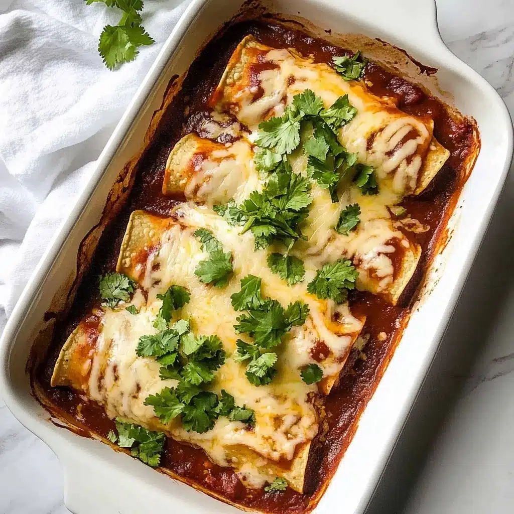 Beef Enchiladas, Beef Enchiladas Recipe, Easy Beef Enchiladas, Homemade Beef Enchiladas, Spicy Beef Enchiladas The image shows a white rectangular baking dish filled with four rolled tortillas covered in a rich reddish-brown sauce. The top layer is melted light yellow cheese that stretches unevenly over the tortillas and sauce. Bright green chopped cilantro is scattered on top, adding a fresh contrast to the warm colors. The dish sits on a white marbled surface next to a soft white cloth.