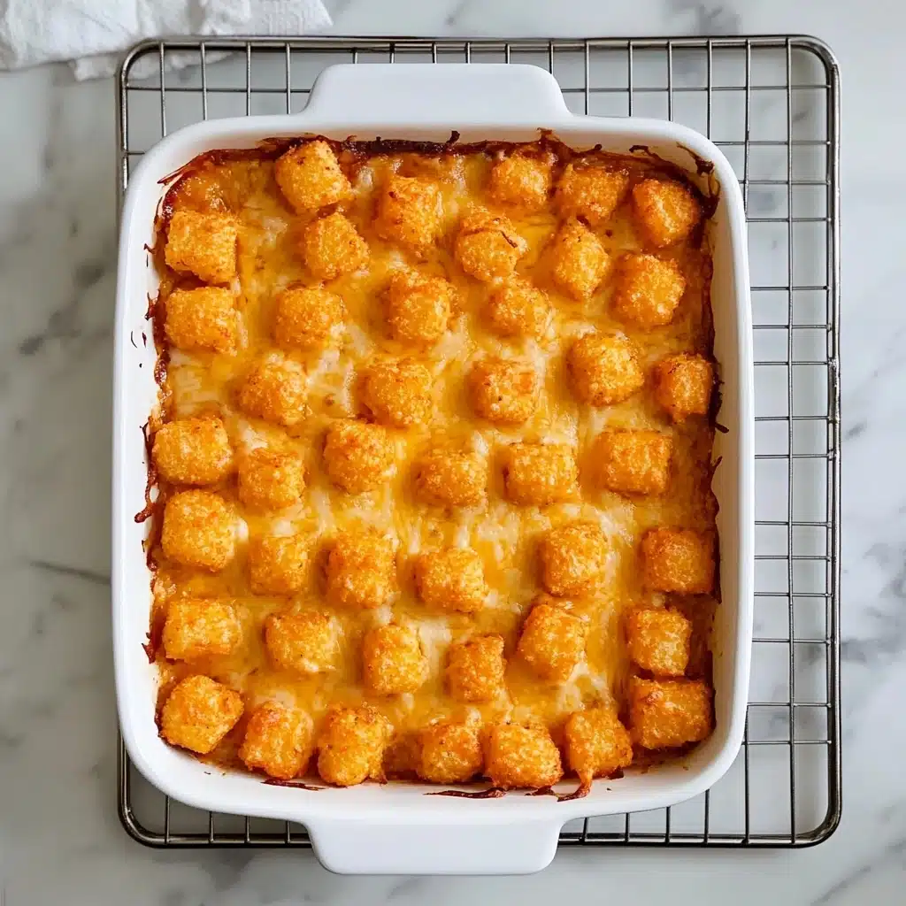 Tater Tot Casserole, easy comfort food, cheesy ground beef casserole, crispy tater tot dinner, quick weeknight casserole A rectangular white ceramic baking dish filled with a single layer of small, square-shaped tater tots that are golden brown and crispy on top, covered in melted orange-yellow cheese. The tater tots are packed closely together, creating an even textured surface, with some cheese slightly browned and bubbling, peeking through the gaps. The dish sits on a small metal cooling rack, which is placed on a white marbled surface.