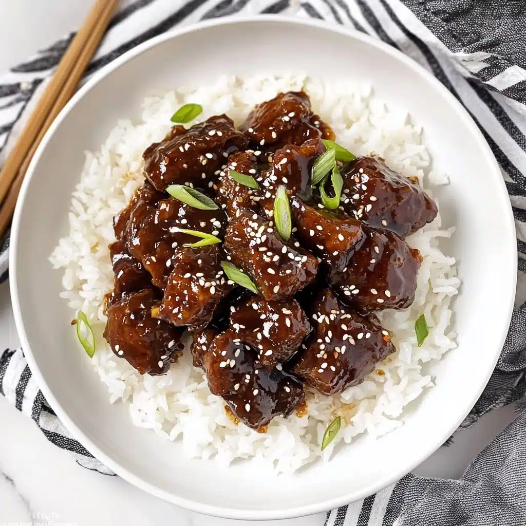 Slow Cooker Korean Beef, Korean Beef Dinner, Easy Korean Beef, Japanese-inspired Beef Slow Cooker, Hearty Asian Beef Stew A white plate with a silver decorative edge holds a serving of white rice as the bottom layer, topped with dark brown glazed pieces of meat covered in a thick sauce. The meat is sprinkled with white sesame seeds and thinly sliced green onions that add a fresh touch on top. The plate is placed on a white marbled surface with a black and white striped cloth nearby.