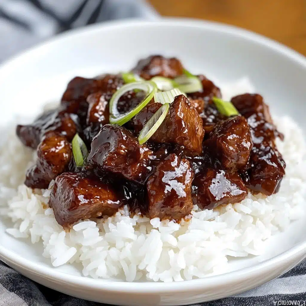 Slow Cooker Korean Beef, Korean Beef Dinner, Easy Korean Beef, Japanese-inspired Beef Slow Cooker, Hearty Asian Beef Stew A white plate with a silver rim holds a bed of fluffy white rice as the bottom layer. On top, there is a thick layer of dark brown glossy meat chunks covered in a rich sauce, creating a shiny texture. The dish is garnished with thin, pale green slices of onion scattered across the meat and rice. To the side of the plate, a silver spoon rests on the white marbled surface.