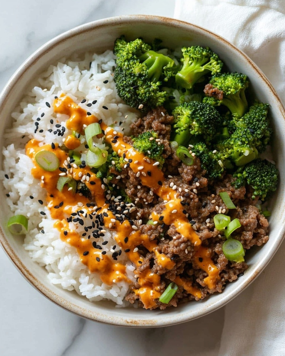 Teriyaki Ground Beef and Broccoli, easy teriyaki beef stir-fry, quick weeknight ground beef recipes, savory broccoli stir-fry, healthy ground beef dinner A round bowl filled with two main parts: a large portion of white rice on the left, topped with small green onion slices, black sesame seeds, and light orange sauce drizzled over it, and on the right, cooked broccoli florets mixed with ground meat, also topped with the same light orange sauce and more green onion slices scattered around. The bowl is placed on a white marbled surface