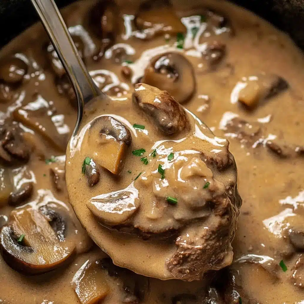 Slow Cooker Beef Stroganoff, Beef Stroganoff, Crockpot Beef Stroganoff, Comfort Food Recipes, Easy Slow Cooker Dinners The image shows a ladle full of creamy brown mushroom sauce with visible chunks of tender beef and sliced mushrooms. The sauce is thick and smooth, coating the ingredients evenly. Small green herb pieces, likely chives, are sprinkled on top of the beef and mushrooms, adding a touch of color. The background is filled with more of the same creamy sauce and mushroom mixture.