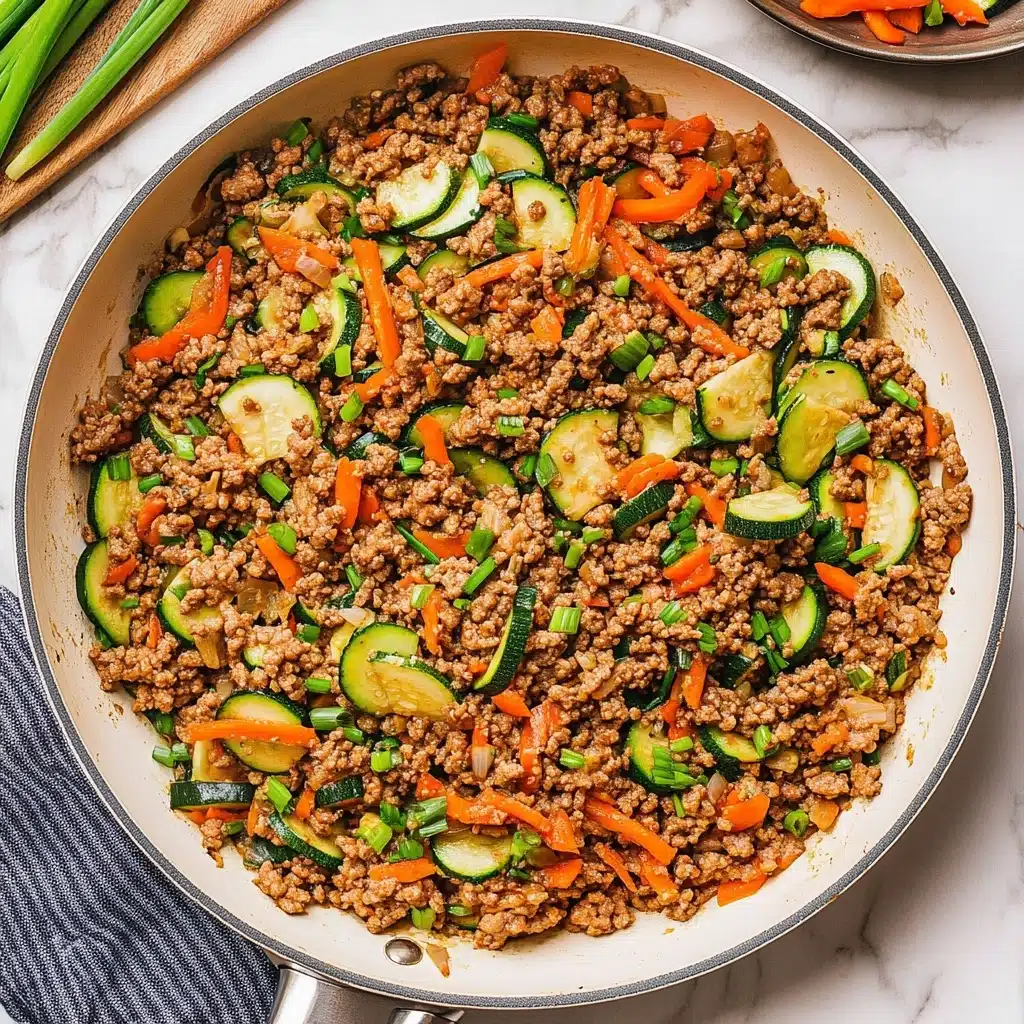 Ground Turkey Stir Fry, healthy ground turkey recipes, quick weeknight dinners, easy stir fry dishes, flavorful turkey stir fry A large white frying pan filled with a mix of cooked ground meat, green zucchini slices, bright orange shredded carrots, and red bell pepper pieces. The ingredients are well mixed, showing a coarse brown texture from the meat, bright green zucchini slices with dark green edges, and scattered pieces of green onion on top. The pan sits on a wooden surface with fresh ginger and carrots beside it, and a white bowl of plain white rice is partially visible in the top right corner.