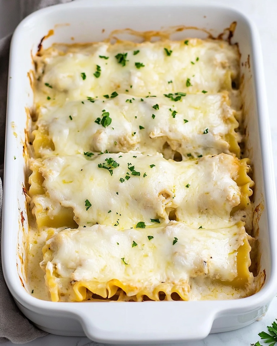 Chicken Alfredo Lasagna Rolls, Alfredo Lasagna Rolls recipe, creamy chicken pasta rolls, cheesy lasagna rolls, easy chicken Alfredo dinner A close-up of a folded lasagna roll held by a woman's hand on a fork, showing three ruffled layers of yellow pasta with white creamy filling inside. The outside is covered in a smooth white sauce sprinkled with small green herb pieces and grated cheese, giving a slightly textured look. The background features more of the lasagna rolls on a white plate with a white marbled surface beneath.