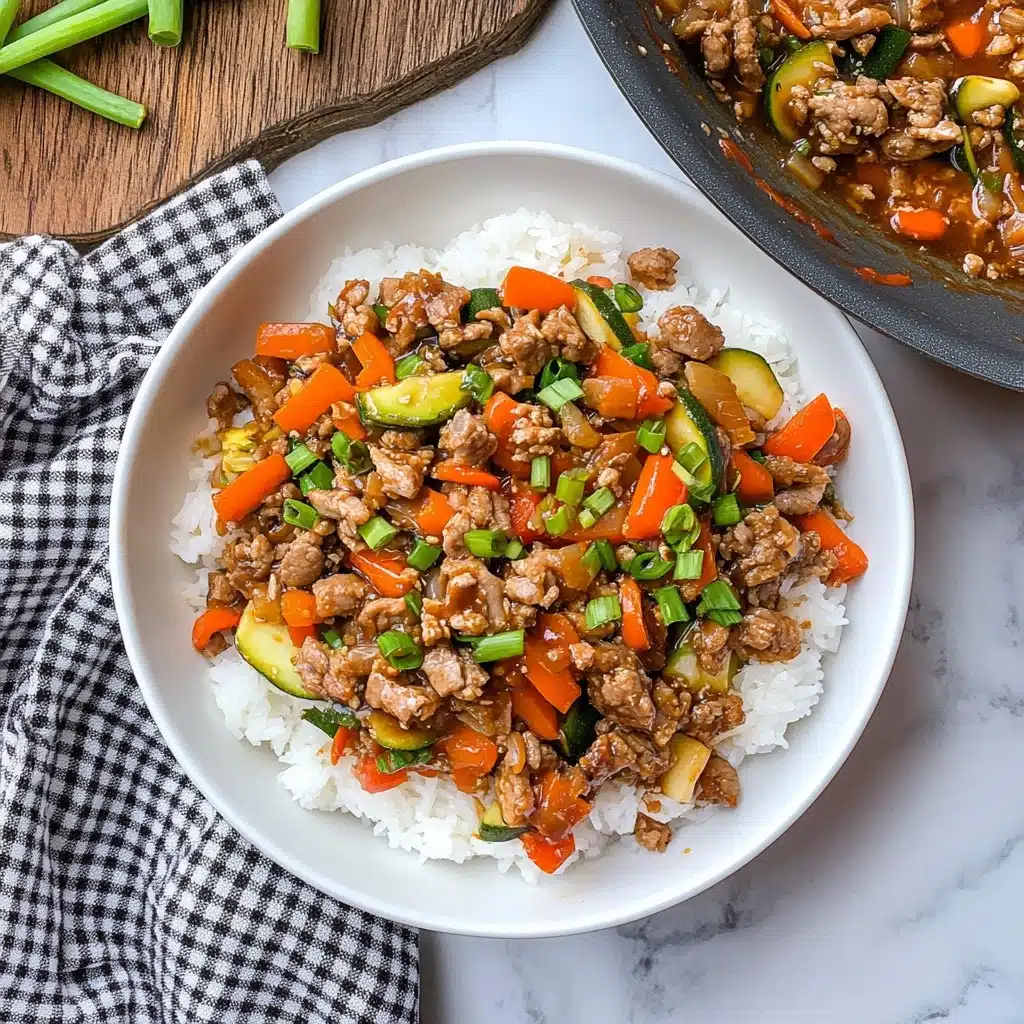 Ground Turkey Stir Fry, healthy ground turkey recipes, quick weeknight dinners, easy stir fry dishes, flavorful turkey stir fry A white bowl filled with a base layer of fluffy white rice, topped with a stir-fry mix of finely chopped cooked meat, bright orange carrot pieces, red bell pepper chunks, and green zucchini slices, garnished with chopped green onion slices scattered on top. To the upper right, a white pan shows the same stir-fry mixture, while fresh vegetables and ginger root lay on a white marbled surface to the top left. A folded checkered cloth is seen to the lower left, and two silver forks rest on the lower right of the wooden surface below.