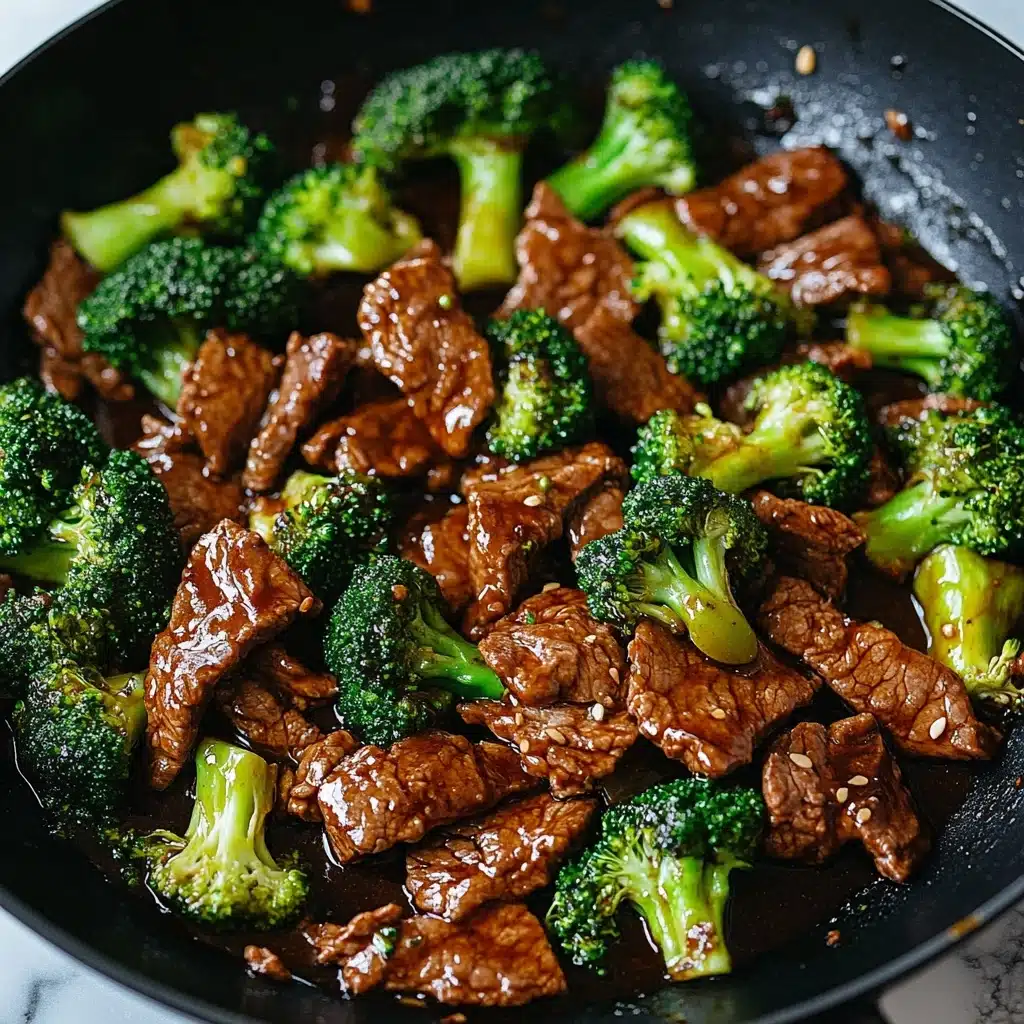 Chinese Beef and Broccoli, Chinese Beef and Broccoli stir-fry, easy Chinese beef recipes, healthy beef stir-fry, quick weeknight dinner recipes This image shows a close-up of beef and broccoli stir-fry in a black pan. The dish has many pieces of thin, brown, cooked beef mixed with bright green broccoli florets, all coated in a shiny, dark brown sauce with small bits of garlic or ginger. The broccoli has a fresh, firm texture and is spread evenly among the beef slices. The black pan contrasts with the colors of the food, and the background is a white marbled texture.