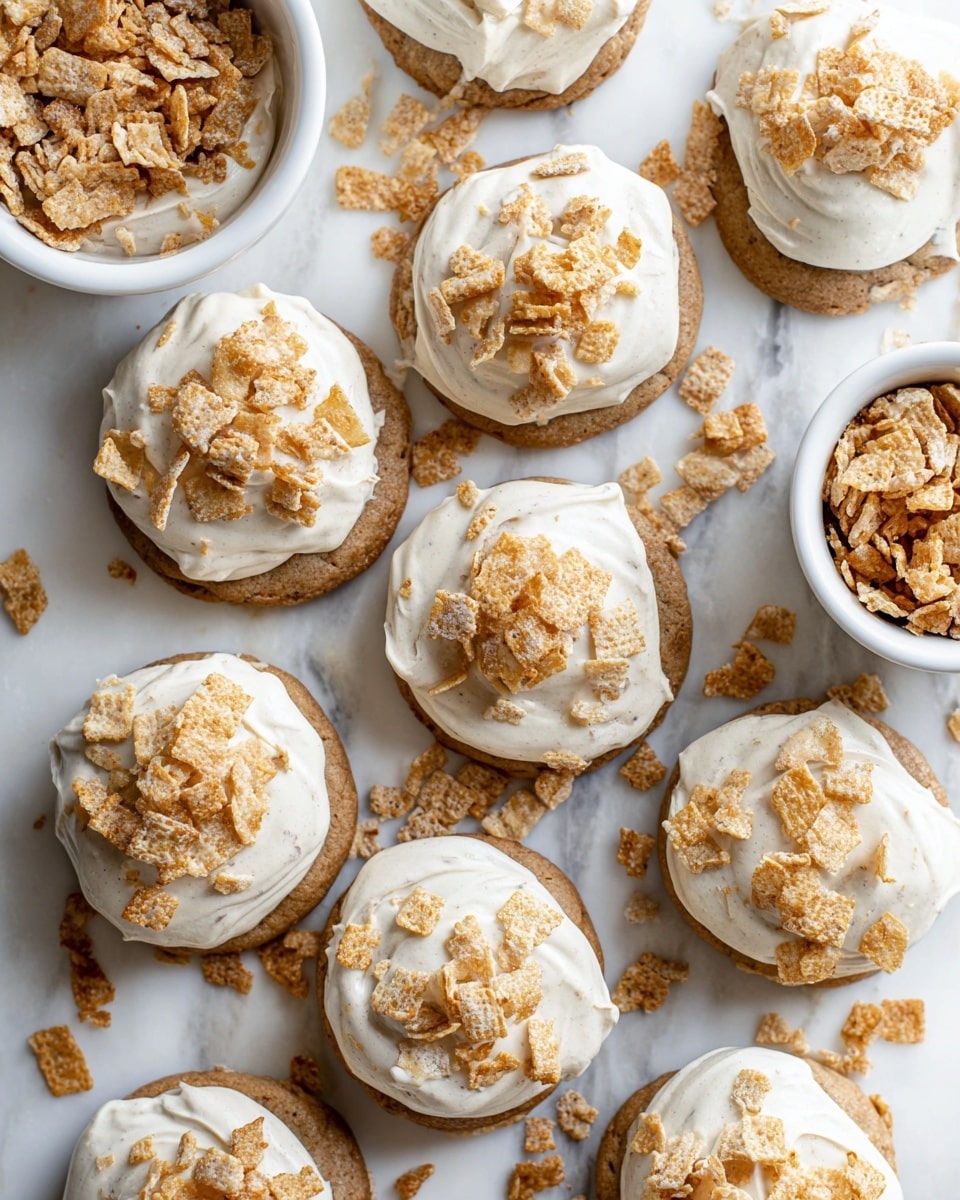 The image shows several cookies arranged on a white marbled surface. Each cookie has two layers: the bottom is a soft brown cookie with a slightly rough texture, and the top layer is a thick white icing spread unevenly. Over the icing, there are crushed light brown cereal flakes scattered, adding a crunchy texture. More crushed flakes are scattered around the cookies on the surface, enhancing the sense of a casual, inviting setting. The focus is on the front cookies with a soft blur on the ones in the back. Photo taken with an iphone --ar 4:5 --v 7