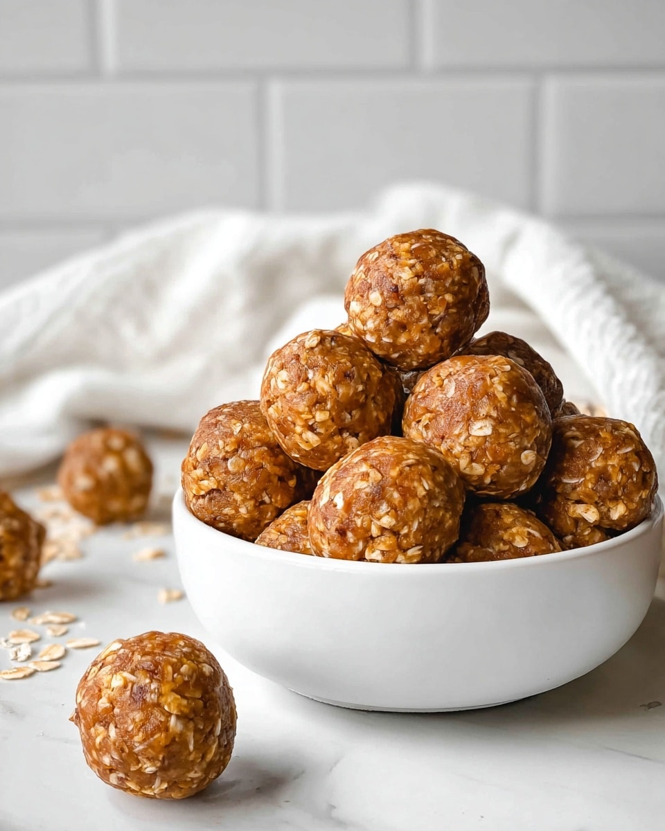 A white bowl is filled with round, brown energy balls that have visible bits of oats inside, stacked neatly with some balls spilling out onto a white marbled surface. The texture looks dense and slightly rough with oats embedded throughout each ball. Behind the bowl, there is a soft white cloth casually draped, and the background features white tiled walls, creating a bright and clean setting. The scene is well lit, highlighting the warm tones and texture of the energy balls. photo taken with an iphone --ar 4:5 --v 7