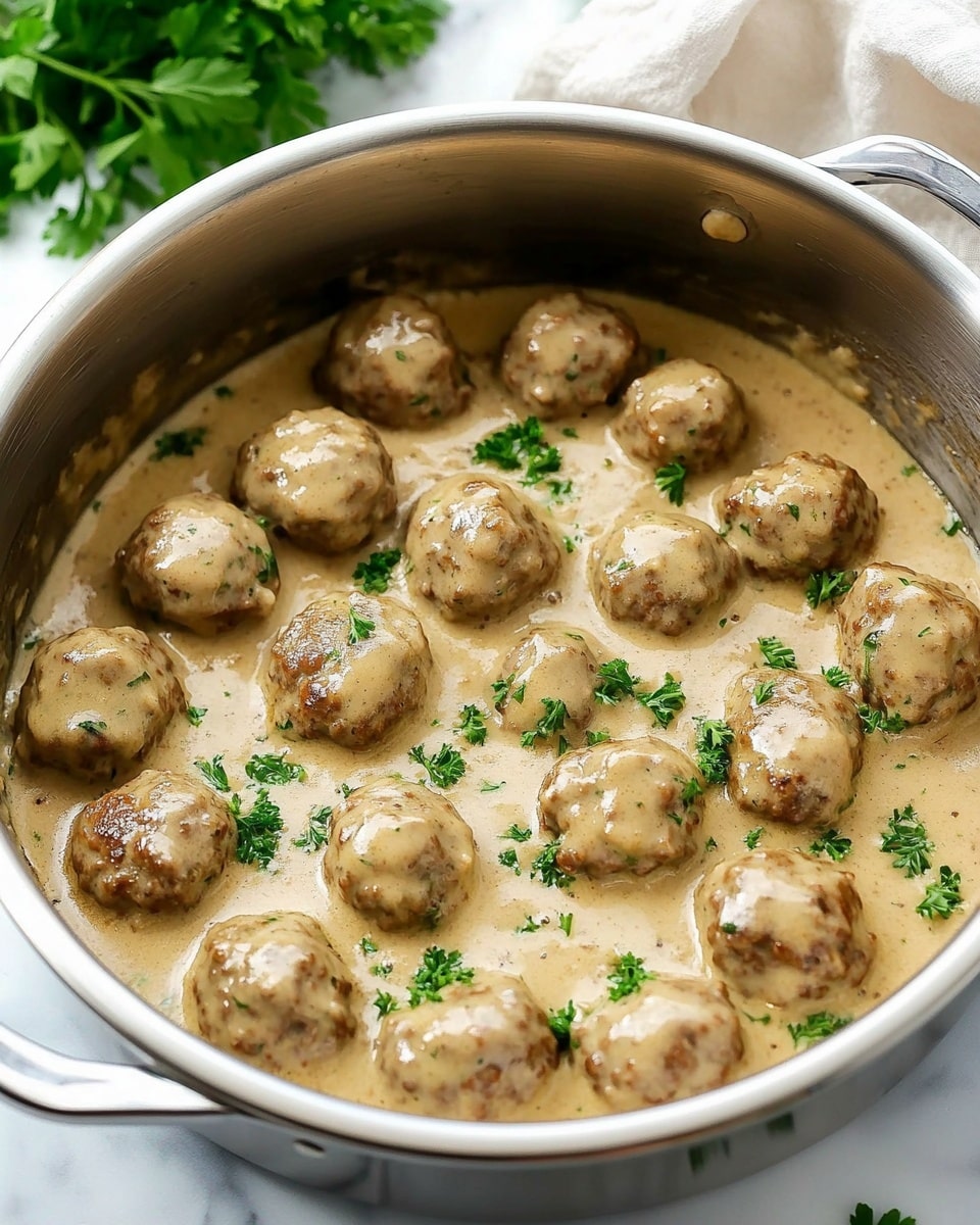 A white bowl on a white marbled surface holds a serving of creamy mashed potatoes topped with eight brown meatballs covered in light brown gravy. The mashed potatoes take up the right side and back of the bowl, showing a smooth and fluffy texture with a few small lumps. The meatballs are placed on the left side, partially resting on the mashed potatoes, and are coated evenly with the gravy that also pools slightly around them. Small green parsley bits are sprinkled on top of the meatballs and sauce, adding color contrast. A silver fork rests on the right inside edge of the bowl, slightly inserted into the mashed potatoes. photo taken with an iphone --ar 4:5 --v 6.1