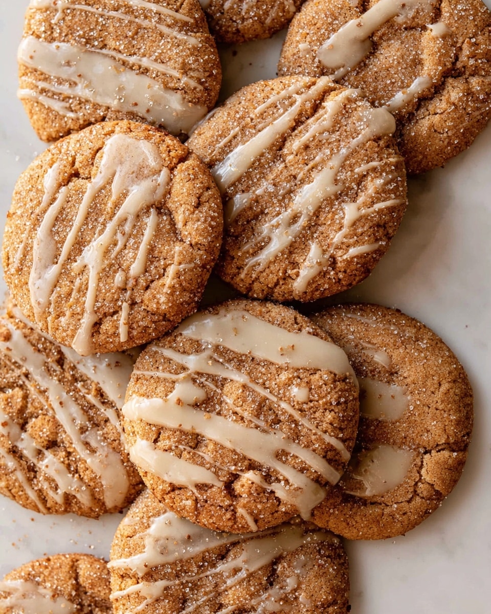 A group of round cookies arranged closely on a white plate on a white marbled surface. There are six cookies visible, each with a brown, slightly rough texture covered in a layer of coarse sugar crystals, giving a sparkly effect. A thin white glaze is drizzled unevenly on top of each cookie, creating light streaks and star-like shapes. In the center, two cookies are stacked with one cookie broken in half, showing a dense, moist interior with the same brown color as the outside. The overall look is warm and inviting, with the contrast between the sparkling sugar, the brown cookie base, and the light glaze. photo taken with an iphone --ar 4:5 --v 7