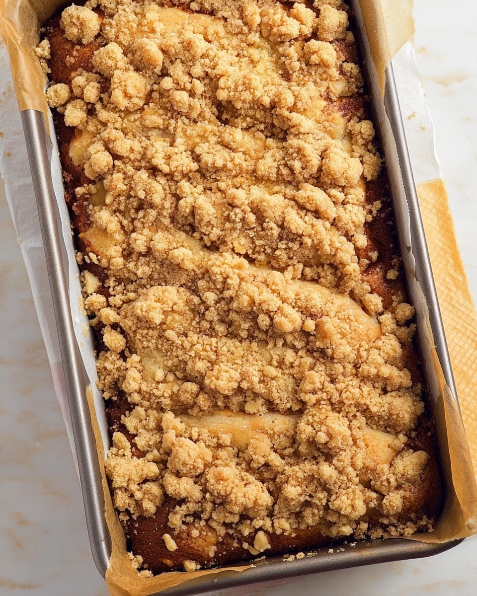 A rectangular metal baking pan is filled with a golden-brown crumb cake. The cake has a textured, crumbly topping layer made up of uneven clusters in light beige and golden colors, scattered thickly across the surface. The cake beneath looks moist and slightly darker, with a soft and fluffy texture visible under the topping. The pan sits on a white marbled surface, and strips of parchment paper extend from the sides inside the pan. The crumb topping is rough and irregular, showing some cracks and crumb pieces scattered around the edges of the cake. Photo taken with an iphone --ar 4:5 --v 7