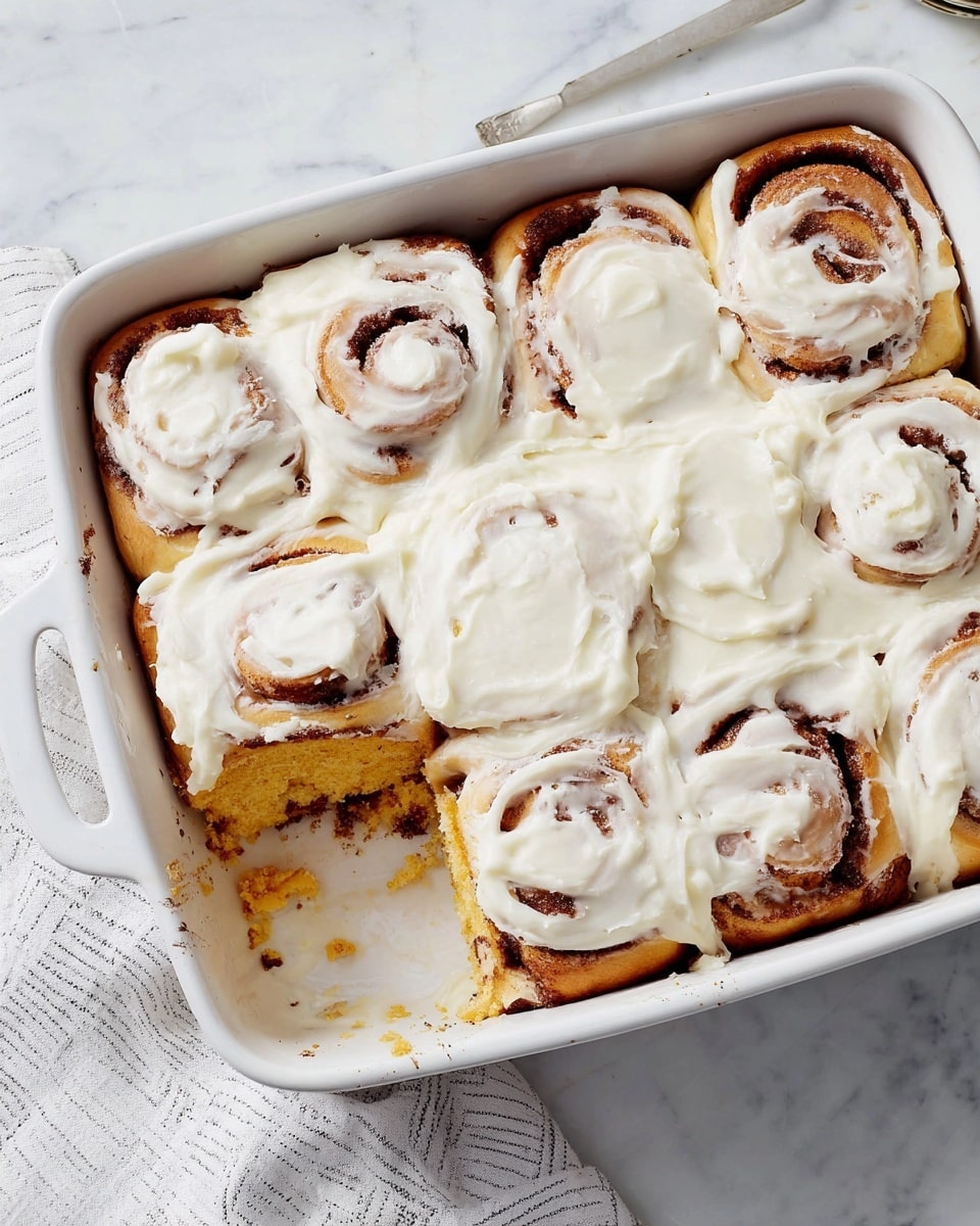 A single square piece of soft cinnamon roll with a light brown baked outer layer and a fluffy, light golden interior. The top is covered with a thick, creamy layer of white cream cheese frosting, swirled smoothly around the edges and slightly dripping down the sides. It sits on a simple white plate placed on a white marbled surface. Photo taken with an iphone --ar 4:5 --v 7