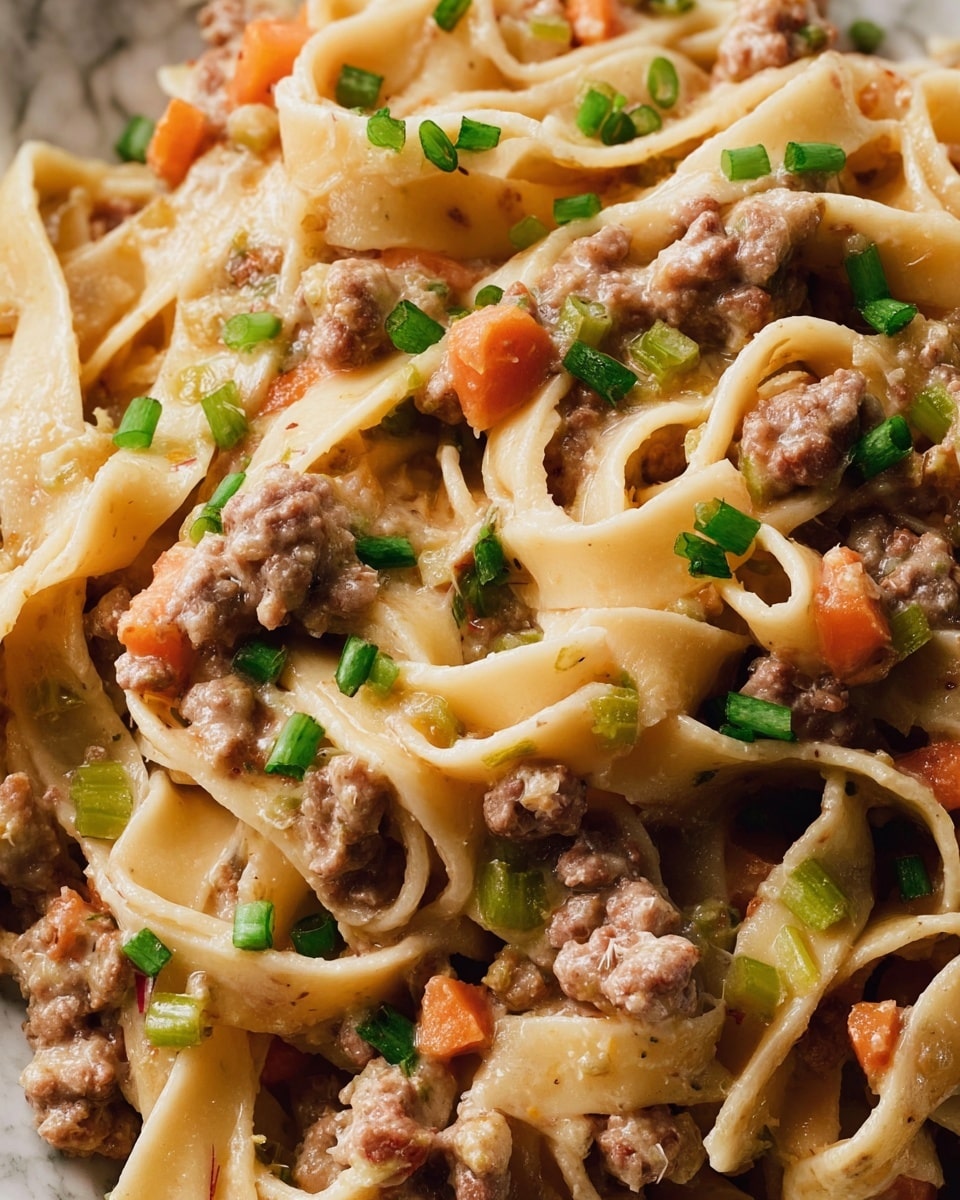 The image shows thick flat pasta noodles mixed closely with a creamy sauce that coats them in a light beige color. Scattered throughout are small chunks of browned ground meat, light brown in color, and tiny pieces of orange carrots and pale green celery adding texture and color. Small slices of green onions are sprinkled on top, brightening the dish with their fresh green shade. The pasta and sauce create a soft, slightly shiny texture that makes the dish look rich and hearty, all on a white marbled surface. photo taken with an iphone --ar 4:5 --v 7