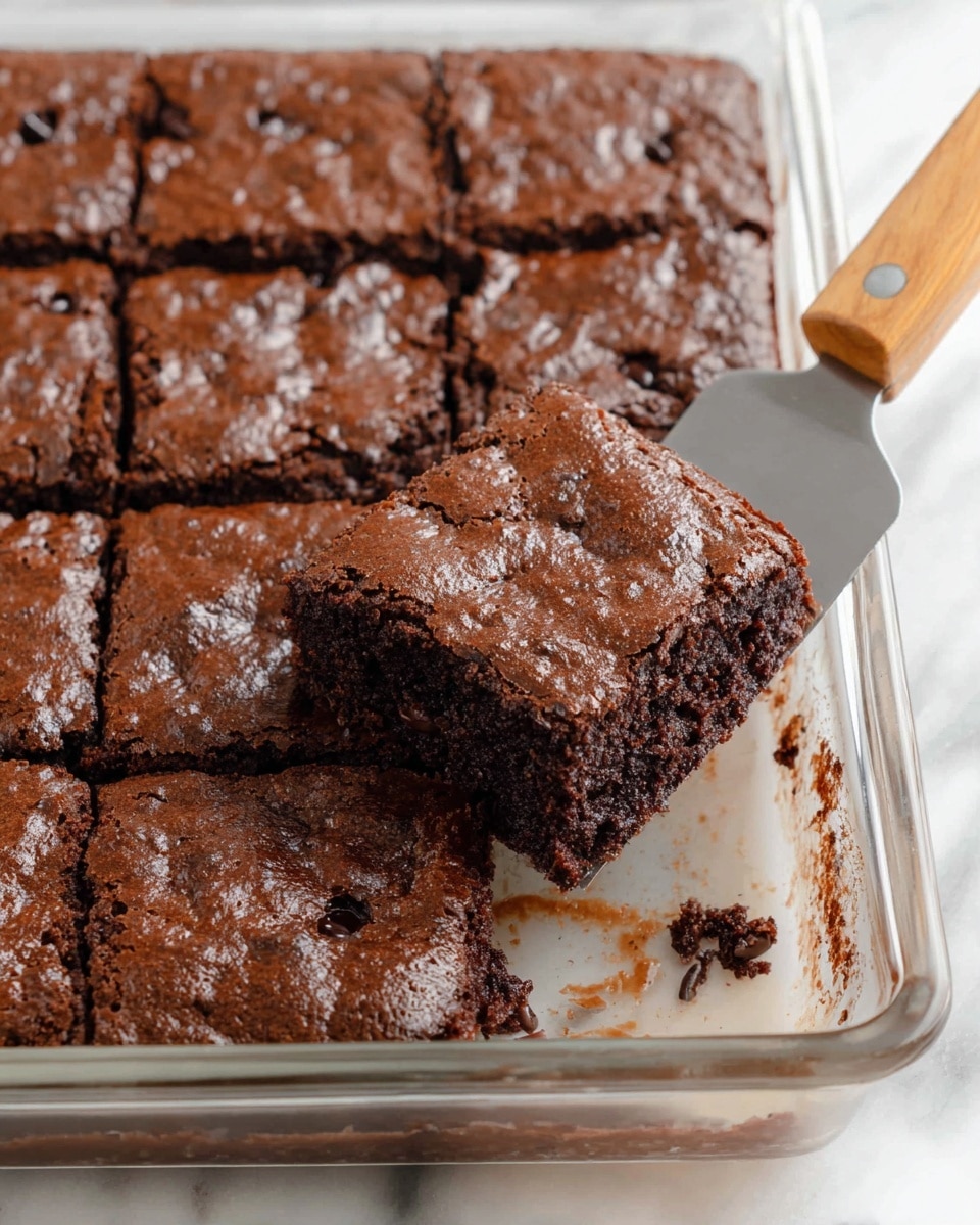 The image shows a single piece of chocolate cake on a white plate placed on a white marbled surface. The cake has two visible layers: the top layer is dark brown and has a slightly cracked, moist texture, while the bottom layer shows a denser, fudgy chocolate inside with small air holes. A fork is placed on the plate, holding a small piece of the cake in front of the main slice. In the background, there is another white plate with a similar piece of cake and two glasses of milk that are softly out of focus. Photo taken with an iphone --ar 4:5 --v 7