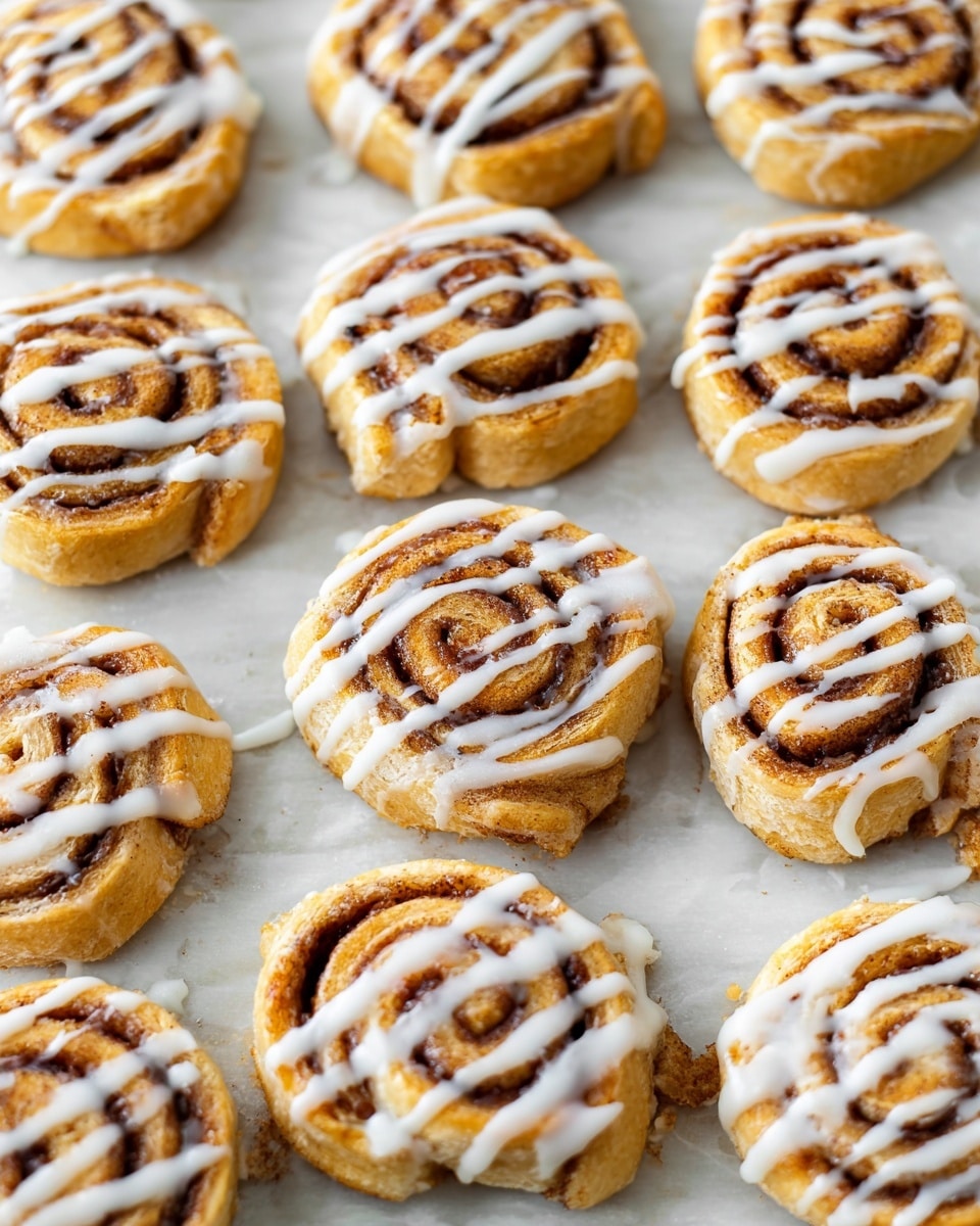 There is a white plate with curved edges holding seven round cinnamon rolls. Each roll has a golden brown dough spiral with dark cinnamon filling. The rolls are topped with thin white icing drizzled in uneven lines over each piece. The plate is placed on a white marbled surface. photo taken with an iphone --ar 4:5 --v 7
