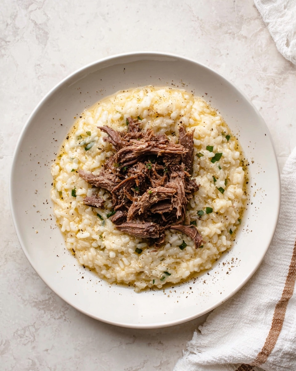 The dish shows two layers on a white plate: the bottom layer is creamy risotto with a pale yellow color mixed with small bits of green herbs and a slightly soft texture, covering most of the plate; the top layer is shredded dark brown meat placed in the center, piled loosely with visible strands and a tender look. A gold fork rests on the right side of the plate, partially on the risotto and meat. The plate is set on a white marbled surface with a soft cloth in the upper right corner. Photo taken with an iphone --ar 4:5 --v 7