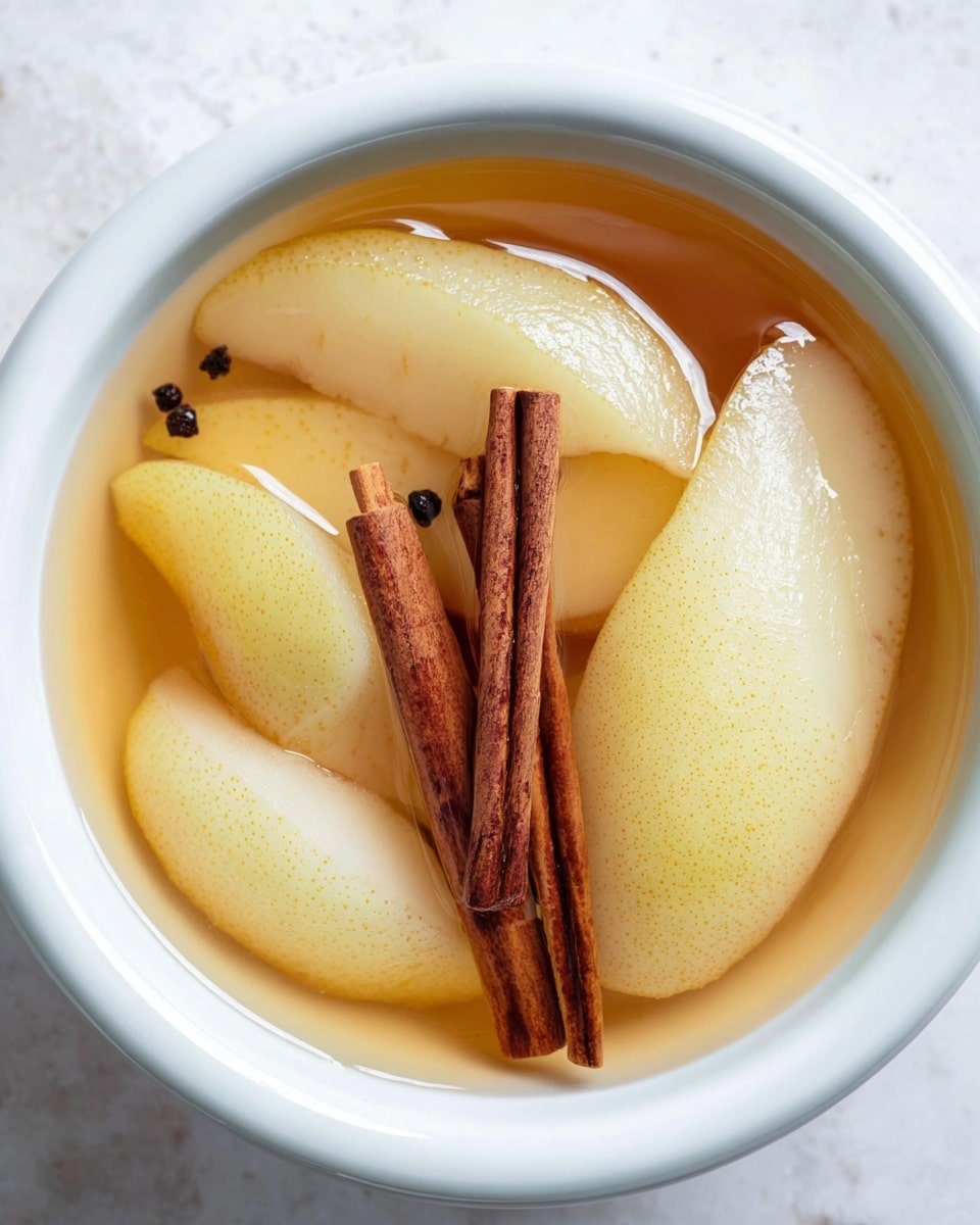The image shows a white bowl filled with a light amber liquid, which looks like syrup or juice. Inside, there are several pale yellow, soft pear slices arranged in a shallow layer. On top of the pear slices, three dark brown cinnamon sticks rest, standing out against the lighter colors. Small black specks, possibly vanilla seeds, scatter throughout the liquid and pears. The bowl sits on a white marbled surface. Photo taken with an iphone --ar 4:5 --v 7