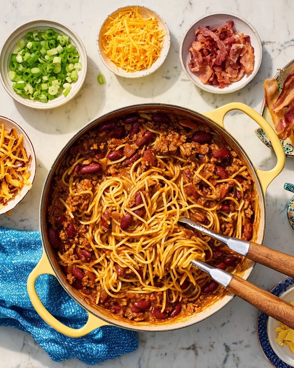 A blue bowl filled with chili spaghetti showing three main layers: a base layer of yellow spaghetti noodles mixed with red kidney beans and ground meat in dark reddish sauce, topped with scattered slices of cooked bacon in light brown, and sprinkled with chopped green onions and shredded yellow cheese on top. A silver fork rests on the right edge of the bowl. To the right, a white plate holds a single golden-brown bread roll. Next to it, a small white bowl contains sliced green onions. The whole setting is on a white marbled surface, with a water glass and bottles of hot sauce nearby. A woman’s hand holds the fork in the bowl. photo taken with an iphone --ar 4:5 --v 7