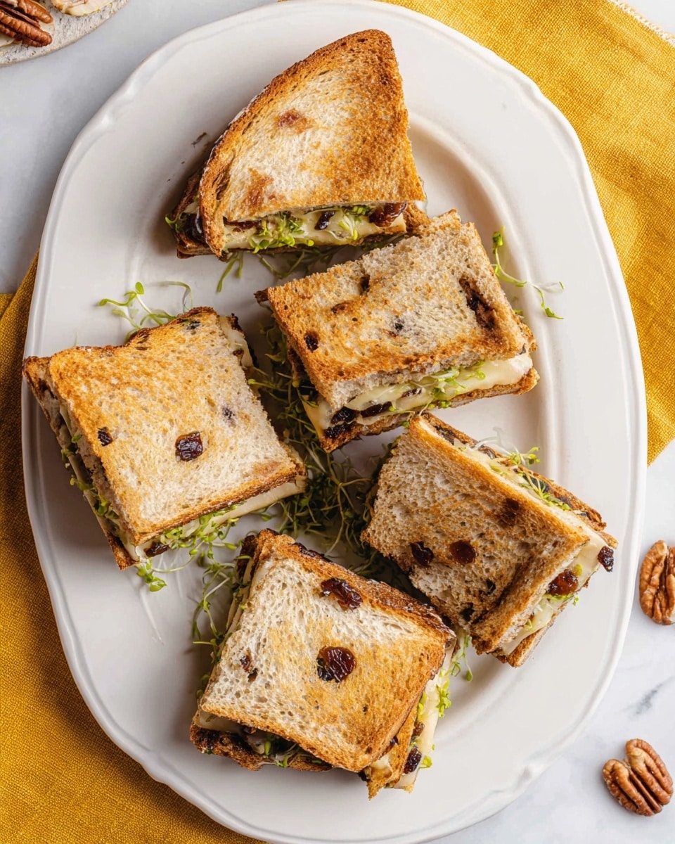 The image shows a white plate with five sandwich quarters arranged casually on it. The sandwiches are made with toasted raisin bread, showing light brown crusts with dark raisin spots. Inside, there are visible layers of melted cheese and fresh green sprouts, giving a mix of creamy white and green textures in the middle. The sandwiches rest on a white marbled surface with a rough yellow cloth seen to the side and some pecans scattered nearby. photo taken with an iphone --ar 4:5 --v 7