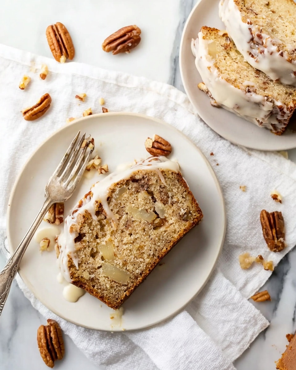 A loaf of light brown cake with visible chunks of apple inside is positioned on a white marbled surface, partially sliced to reveal its soft, moist texture. The top is covered with a slightly thick layer of creamy, off-white icing that drips down the sides and is sprinkled with small pieces of nuts. The cake rests on a cooling rack over white parchment paper with crumb bits scattered around. In the blurred background, there are two green apples. Photo taken with an iphone --ar 4:5 --v 7