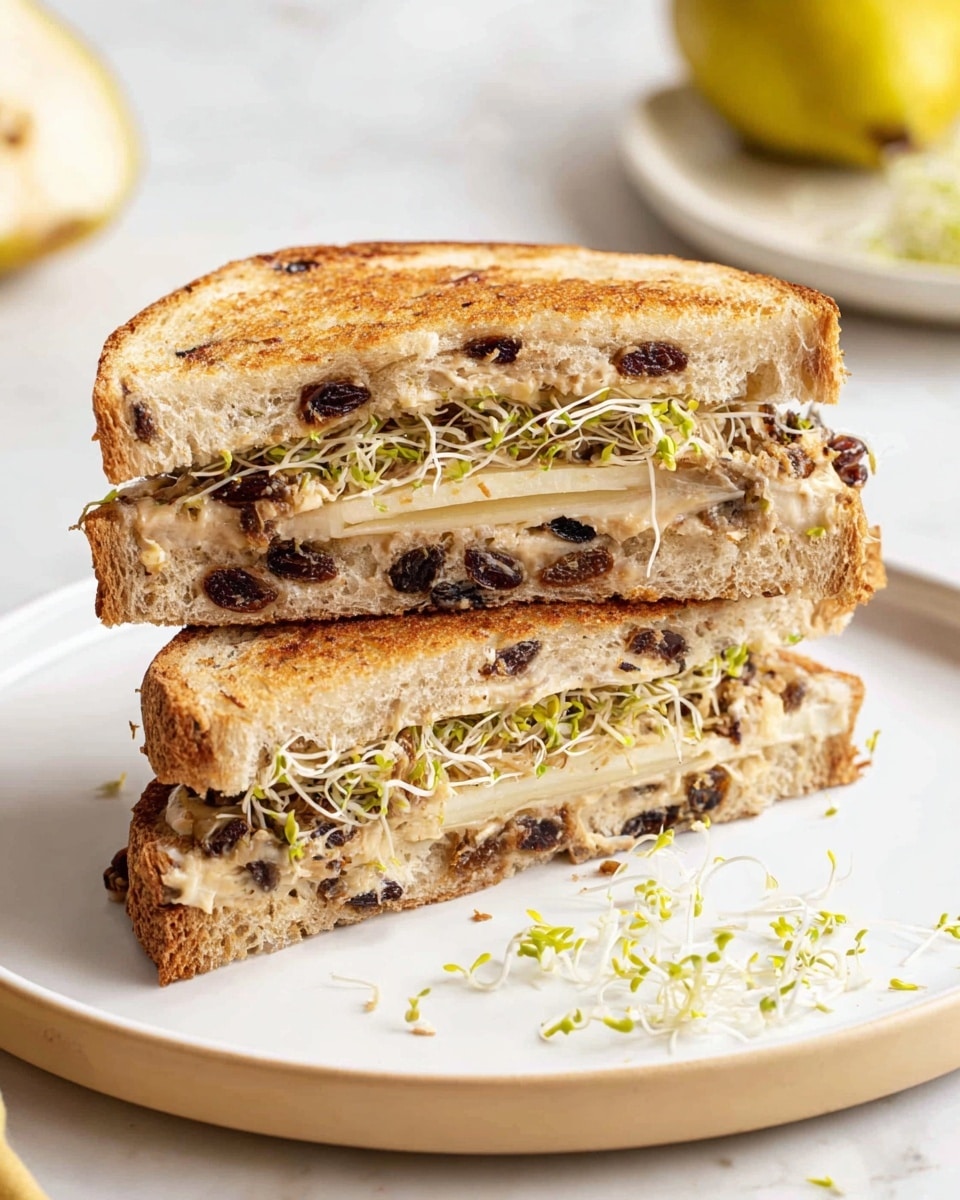 The image shows a stack of small, square sandwiches arranged on a white plate with a white marbled surface in the background. Each sandwich has three layers: the top and bottom layers are toasted raisin bread with a light brown, slightly crunchy texture with visible raisins, and the middle layer contains a creamy spread and fresh alfalfa sprouts with thin, green and white strands peeking out. The sandwiches appear soft inside with a crisp crust outside, stacked unevenly but neatly, highlighting the contrast between the bread's toasted golden brown color and the fresh light green sprouts. photo taken with an iphone --ar 4:5 --v 7