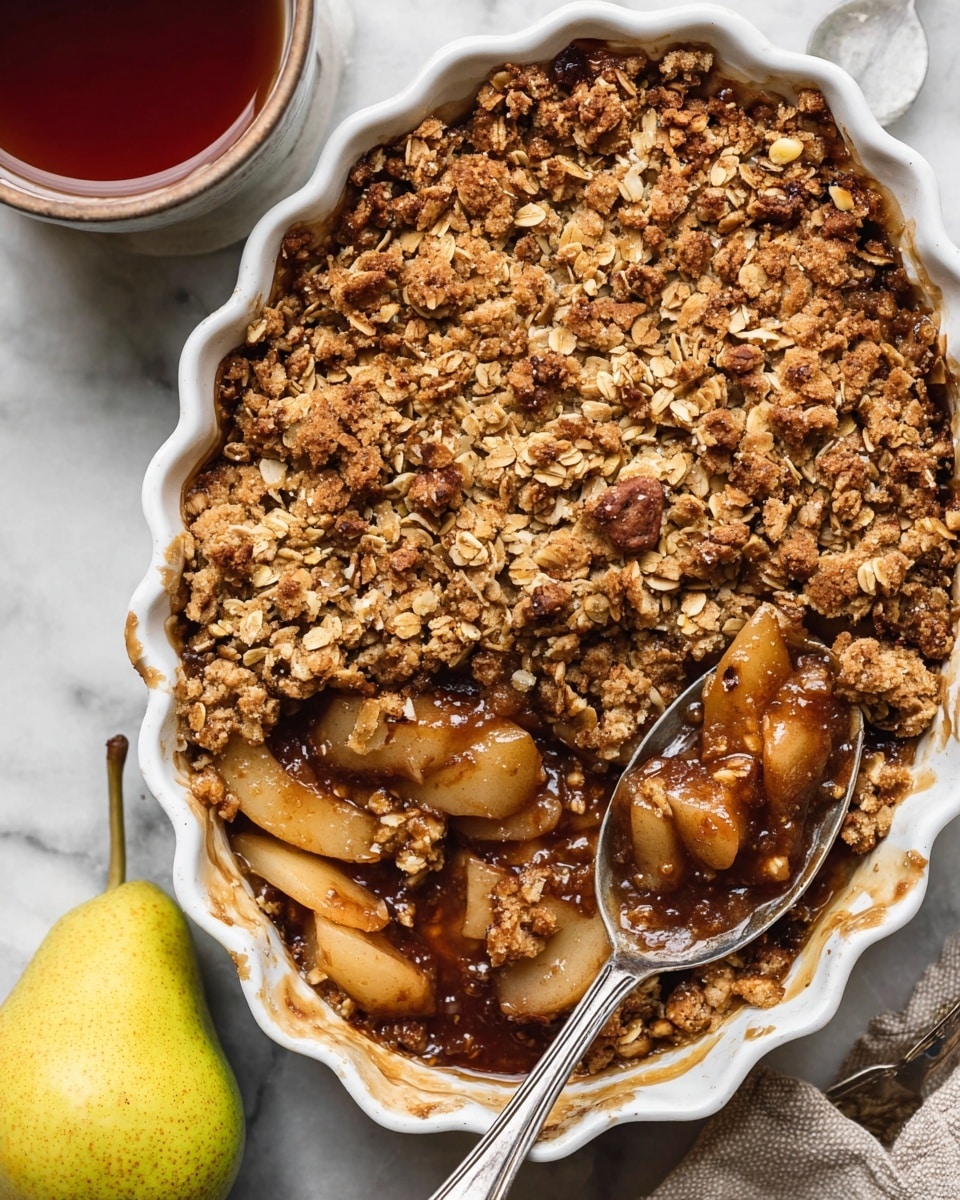 A white scalloped-edge baking dish filled with a pear crumble is shown from above, featuring two layers: the bottom layer shows soft, sliced pear pieces coated in a shiny, dark cinnamon-spiced sauce, while the top layer consists of a rough, golden-brown oat crumble with visible oats and small nut bits that look crunchy. A large silver spoon rests on the right side inside the dish, holding a scoop of both layers. The dish is placed on a white marbled surface, with a yellow pear and a cup of tea nearby. Photo taken with an iphone --ar 4:5 --v 7
