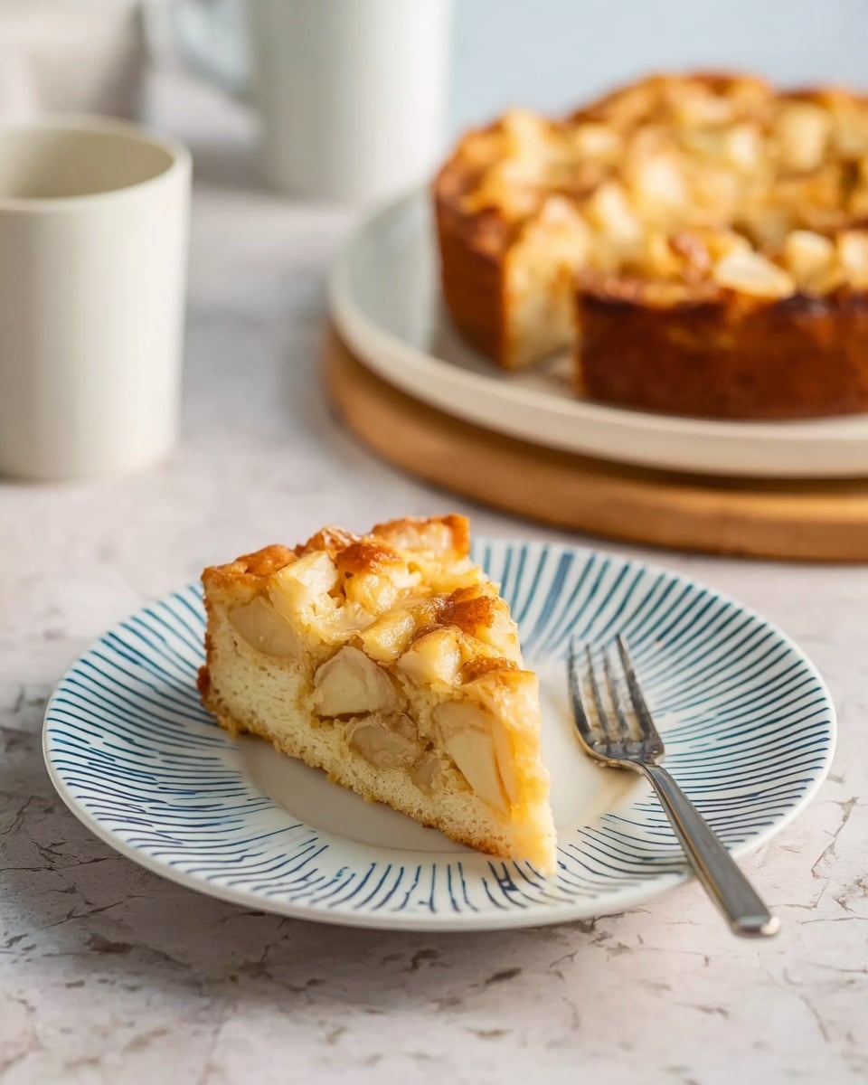 The image shows a round apple pie with a golden brown crust on a white plate placed on a wooden board. The pie is topped with small cubes of baked apple, giving a textured appearance. One slice is removed and placed on a white plate with blue stripes along the edge. The slice reveals a creamy, light filling beneath the apple cubes. A silver fork rests on the edge of the smaller plate. A cup of light-colored drink, possibly coffee or tea, is also visible in the background. The scene is set on a white marbled surface with a blue and white checked cloth partially visible. Photo taken with an iphone --ar 4:5 --v 7