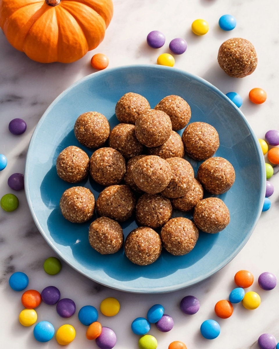 A round white plate holds about twenty small, round, brown balls with a rough texture, arranged closely together. The plate sits on a light blue tray, surrounded by small, colorful candy-coated pieces in red, orange, yellow, green, blue, and purple scattered around the plate and tray. In the top background, there is a small, bright orange pumpkin. The whole scene is set on a white marbled surface. photo taken with an iphone --ar 4:5 --v 7