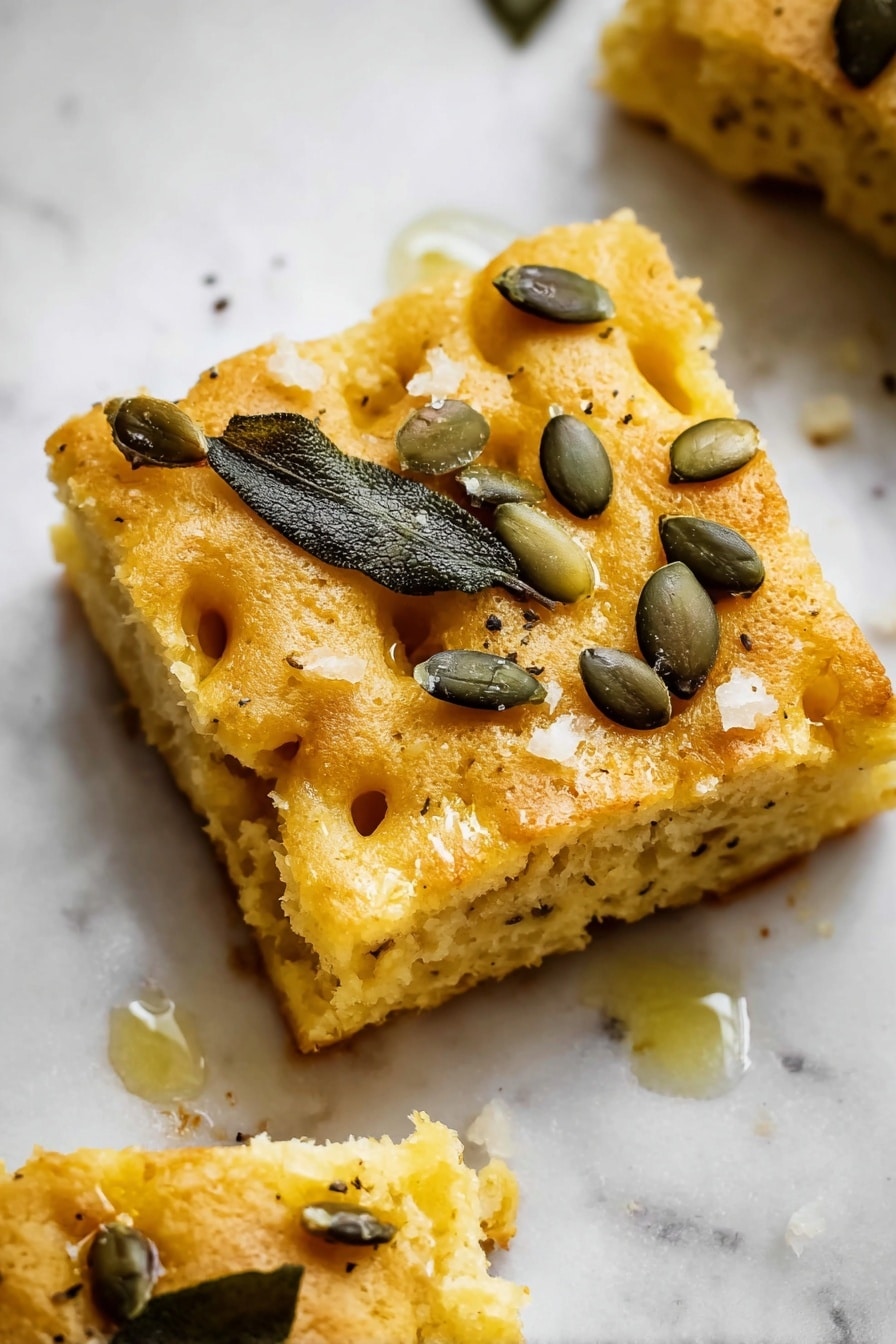 The image shows a close-up view of a single-layer focaccia bread with a yellowish, soft, and slightly bumpy texture. The surface of the bread is scattered with small, green pumpkin seeds and sprinkled lightly with coarse salt. Dark green, almost black, sage leaves are placed evenly on top, adding contrast to the golden color of the bread. The irregular indentations on the dough give depth to the image, highlighting the spongy texture. The photo was taken on a white marbled surface photo taken with an iphone --ar 2:3 --v 7 - Pumpkin Sage Focaccia, Pumpkin Sage Focaccia with Pepitas and Parmesan, Autumn Focaccia Recipe, Savory Pumpkin Bread, Easy Fall Bread