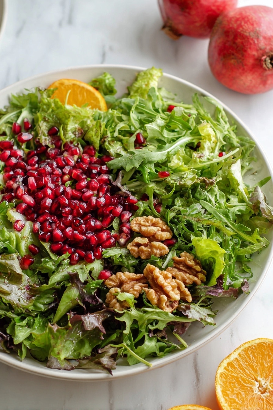 A fresh mixed green salad is shown on a white plate on a white marbled surface. The salad has three main layers: the bottom layer is a mix of different green leafy vegetables including light green lettuce and dark green arugula. The middle layer is bright red pomegranate seeds scattered evenly across the greens. The top layer features brown walnut pieces placed over the pomegranate seeds and greens. On one side of the plate, there is a small orange slice adding a bit of color contrast. In the background, two whole pomegranates are partially visible on the white marbled surface. photo taken with an iphone --ar 2:3 --v 7 - Pomegranate Greens Salad with Halloumi Croutons and Spiced Orange Vinaigrette, healthy vegan salad recipes, fresh fruit and cheese salad, easy citrus vinaigrette salad, vibrant winter green salad