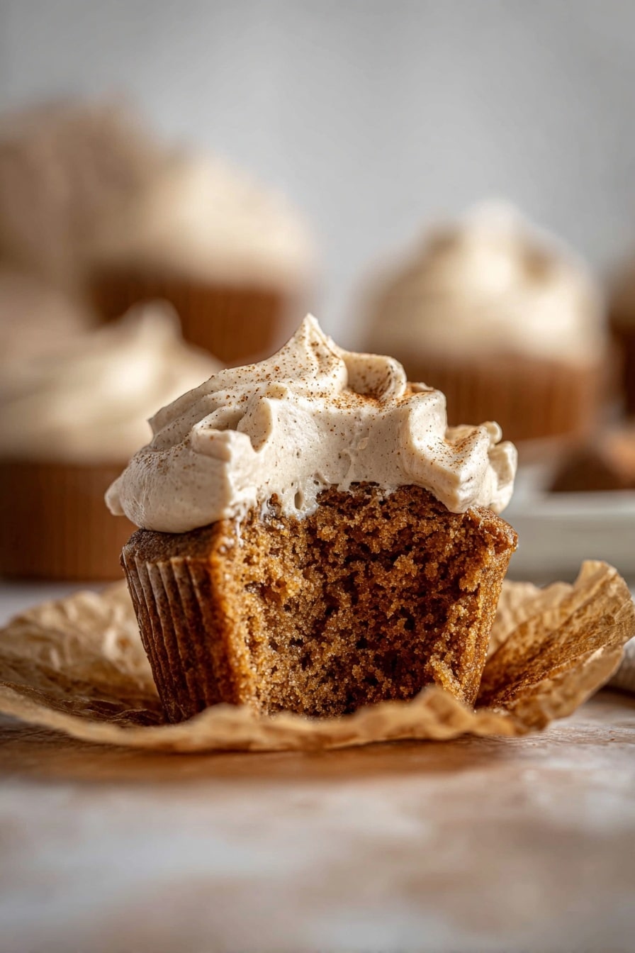Seven cupcakes sit closely together, each wrapped in light brown parchment paper. Four of the cupcakes have a smooth, swirled layer of creamy white frosting on top, sprinkled lightly with fine brown powder like cinnamon. The other three cupcakes show their soft, brown cake tops, textured with slight cracks. The cupcakes are on a white marbled surface, filling the frame. Photo taken with an iphone --ar 2:3 --v 7 - Pumpkin Dream Cupcakes with Espresso Cream Cheese Frosting, pumpkin spice cupcakes, fall dessert recipes, coffee-flavored cupcakes, cozy autumn treats