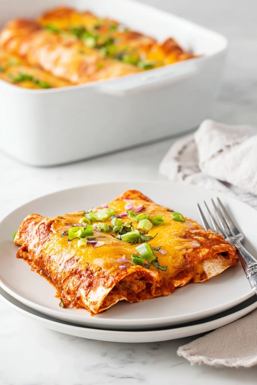 A white baking dish holds three enchiladas covered with dark red sauce and melted yellow and white cheese, forming a thick, textured top layer. The enchiladas underneath have a soft, slightly wrinkled brown tortilla surface, visible where one piece is gently lifted from the corner. Bright green chopped onions are sprinkled evenly on top, adding a fresh color contrast. The dish sits on a white marbled surface and looks warm and inviting. Photo taken with an iphone --ar 2:3 --v 7 - Healthy Leftover Turkey Enchiladas, turkey enchiladas recipe, healthy turkey dinner ideas, quick turkey leftover recipe, nutritious enchiladas