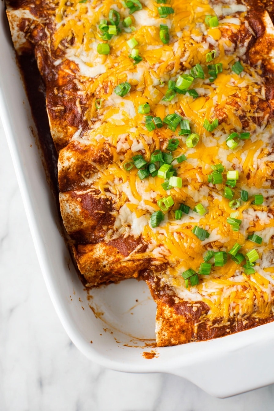 A single rolled enchilada sits in the middle of a clean white plate, topped with melted yellow-orange cheese and sprinkled with chopped green onions. The enchilada itself is covered in a reddish-orange sauce with a slightly thick texture. The edges show soft tortilla layers folded over, revealing a dense filling inside. A silver fork rests on the right side of the plate, and underneath is a stack of white plates on a white marbled surface. In the background, a white casserole dish holds several enchiladas covered with the same melted cheese and garnished with green onions, slightly blurred for depth. photo taken with an iphone --ar 2:3 --v 7 - Healthy Leftover Turkey Enchiladas, turkey enchiladas recipe, healthy turkey dinner ideas, quick turkey leftover recipe, nutritious enchiladas