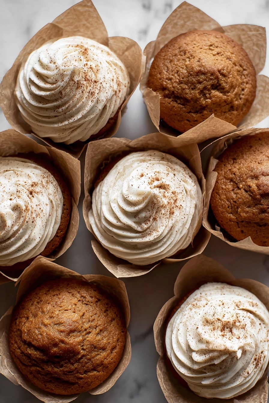 The image shows a close-up of a brown muffin with a soft, moist texture visible inside, as it is split open in the center. On top, there is a thick layer of light beige frosting with a creamy, whipped appearance and small specks of spice sprinkled over it. The muffin sits on a piece of crumpled brown parchment paper, all set against a white marbled surface. In the blurred background, there are more muffins with the same frosting, completing a warm and inviting scene. photo taken with an iphone --ar 2:3 --v 7 - Pumpkin Dream Cupcakes with Espresso Cream Cheese Frosting, pumpkin spice cupcakes, fall dessert recipes, coffee-flavored cupcakes, cozy autumn treats