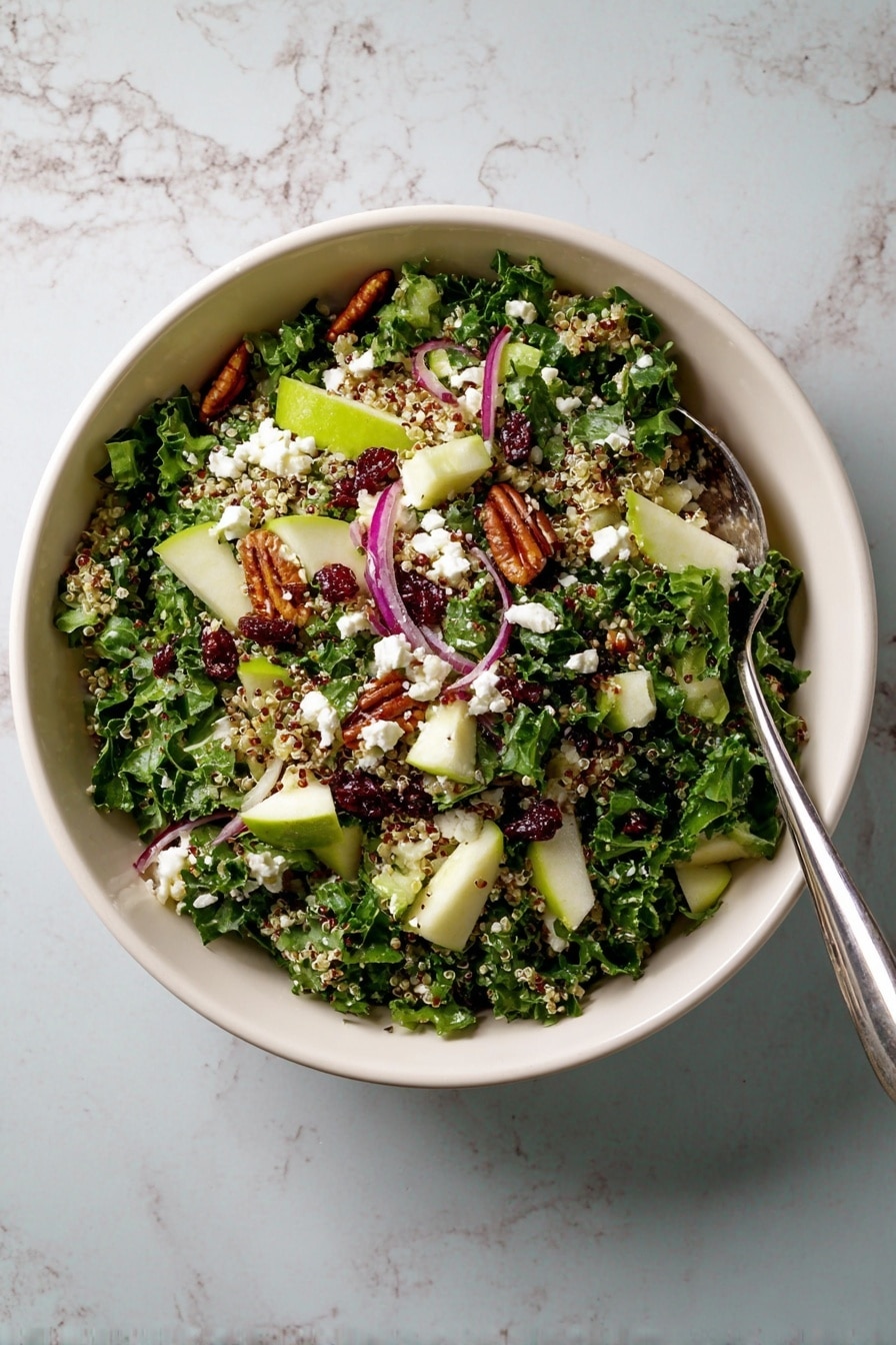 A large white bowl holds a fresh salad with four main layers: the base layer is dark green kale leaves with a rough texture, mixed evenly throughout. On top, there are pale green apple chunks with smooth skin and small white quinoa grains scattered across. Thin curved slices of light purple onion are spread out, adding bright color contrast. Dark red dried cranberries and small brown glazed pecans are sprinkled on top, along with soft white crumbled cheese pieces. A silver fork rests inside the bowl, partially submerged in the salad. The bowl sits on a surface with a white marbled texture. photo taken with an iphone --ar 2:3 --v 7 - Cranberry Apple Quinoa Salad, healthy quinoa salad with cranberries and apples, vegan cranberry apple salad, colorful fruit quinoa salad, nutritious side dish with quinoa and kale