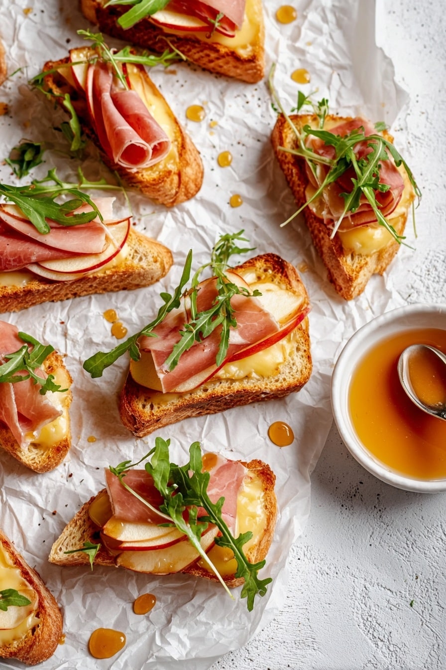 There are seven pieces of golden toasted baguette slices arranged on a white plate with slight ridges. Each toast has a layer of melted light yellow cheese at the bottom, topped with thin slices of pale pink ham and thin slices of light red apples. Green arugula leaves are placed on top of each toast, adding a fresh look. Some black pepper is sprinkled over the toasts, and a few drops of a brown dressing are visible on the plate and toasts. The plate sits on a white marbled surface with a portion of a beige cloth napkin showing at the edge. Photo taken with an iphone --ar 2:3 --v 7 - Apple & Brie Crostini with Hot Honey, Apple Brie Crostini appetizer, easy fruit and cheese crostini, hot honey fruit appetizer, elegant snack ideas