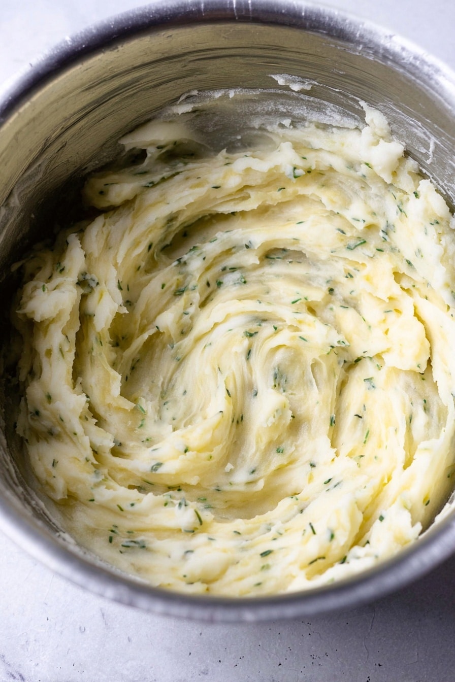 A close-up view of a shiny metal bowl filled with creamy mashed potatoes mixed with small green herb pieces, showing soft swirls and smooth texture inside the bowl, which sits on a white marbled surface photo taken with an iphone --ar 2:3 --v 7 - Instant Pot Mashed Potatoes with Greek Yogurt, Healthy Mashed Potatoes, Quick Mashed Potatoes, Creamy Mashed Potatoes with Parmesan, Easy Instant Pot Potato Recipe