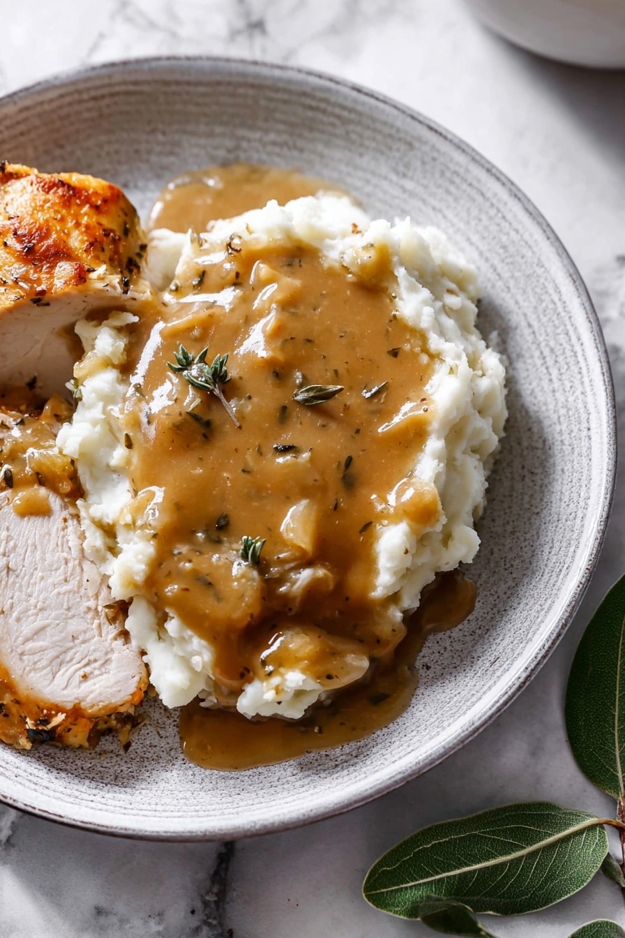 The dish is served on a white plate with a textured look, featuring a layer of smooth white mashed potatoes topped with a thick, brown gravy that has visible bits of herbs and onions, covering the top and slightly running over the sides. Next to the mashed potatoes are slices of cooked white meat with a light brown roasted crust, some also covered with the same brown gravy. The plate is placed on a white marbled surface with a few green leaves positioned near the bottom right corner. Photo taken with an iphone --ar 2:3 --v 7 - Turkey Gravy, Turkey Gravy Tips, Best Turkey Gravy, Easy Turkey Gravy, Homemade Turkey Gravy