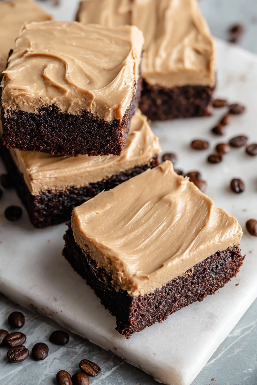 A white plate holds five square dessert bars, each with two layers: a thick, dark brown base layer with a chewy texture and a smooth, light tan frosting layer on top with visible soft streaks. The plate sits on a folded white cloth with dark red stripes, placed on a white marbled surface. In the background, there are some scattered coffee beans and a white cup filled with dark coffee, partially visible at the top left. photo taken with an iphone --ar 2:3 --v 7 - Frosted Coffee Brownies, coffee brownies with frosting, chocolate coffee dessert, mocha brownies recipe, fudgy coffee brownies
