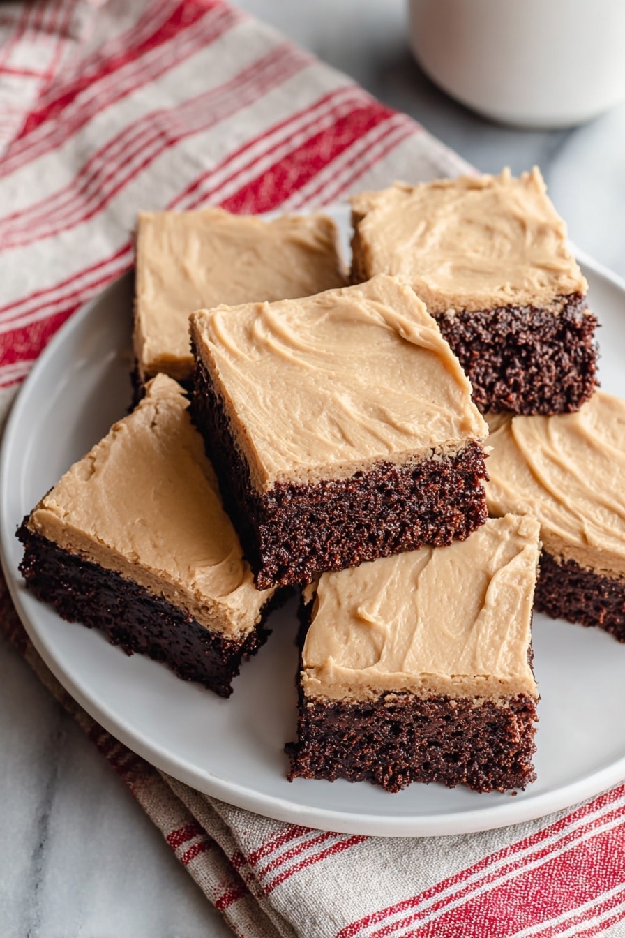 The image shows six square brownies stacked on a white plate, each with two layers: a thick, textured dark brown bottom layer and a smooth, light tan creamy top layer. The brownies have clean edges and the top layer has slight horizontal lines from spreading. The background features a white marbled texture, a white cup, and a fabric with red and white stripes. The photo taken with an iphone --ar 2:3 --v 7 - Frosted Coffee Brownies, coffee brownies with frosting, chocolate coffee dessert, mocha brownies recipe, fudgy coffee brownies