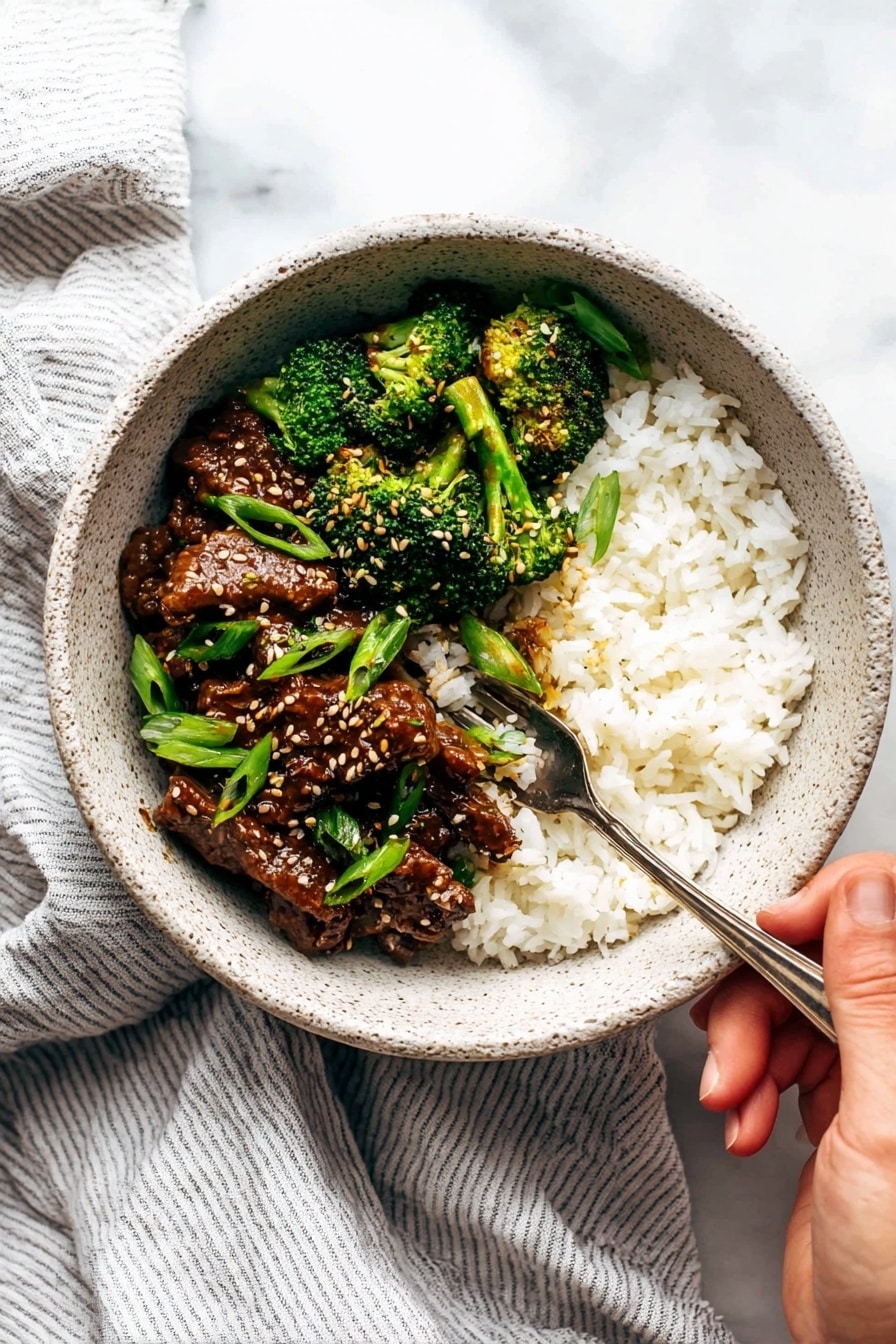 A bowl shows two main layers: bright white rice filling half of the right side, and a mix of dark brown cooked beef pieces with bright green broccoli florets on the left side. The beef is glossy with sesame seeds sprinkled on top, and there are long, thin green onion pieces scattered throughout. A silver fork is placed in the rice, held by a woman's hand at the bottom right corner. The bowl is speckled light grey with a rough texture, sitting on a light grey striped cloth over a white marbled surface. photo taken with an iphone --ar 2:3 --v 7 - Sesame Beef and Broccoli Stir Fry, quick beef stir fry, healthy Asian stir fry, easy beef and broccoli recipe, flavorful stir fry dinner