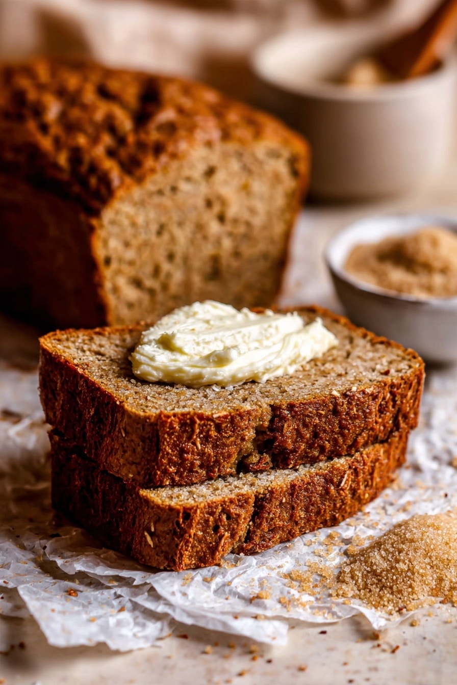 Two thick slices of brown bread with a rough, crunchy crust are stacked on a white marbled surface covered with crumpled parchment paper. The top slice holds a dollop of creamy, white butter. Behind the slices is the rest of the loaf, showing a textured, dense inside with visible small air holes. Around the bread are scattered crumbs and a small white bowl filled with brown sugar. The scene is close-up and softly lit, highlighting the warm brown and beige tones of the bread. Photo taken with an iphone --ar 2:3 --v 7 - Moist Banana Bread, moist banana bread, banana bread recipe, soft banana bread, easy banana bread