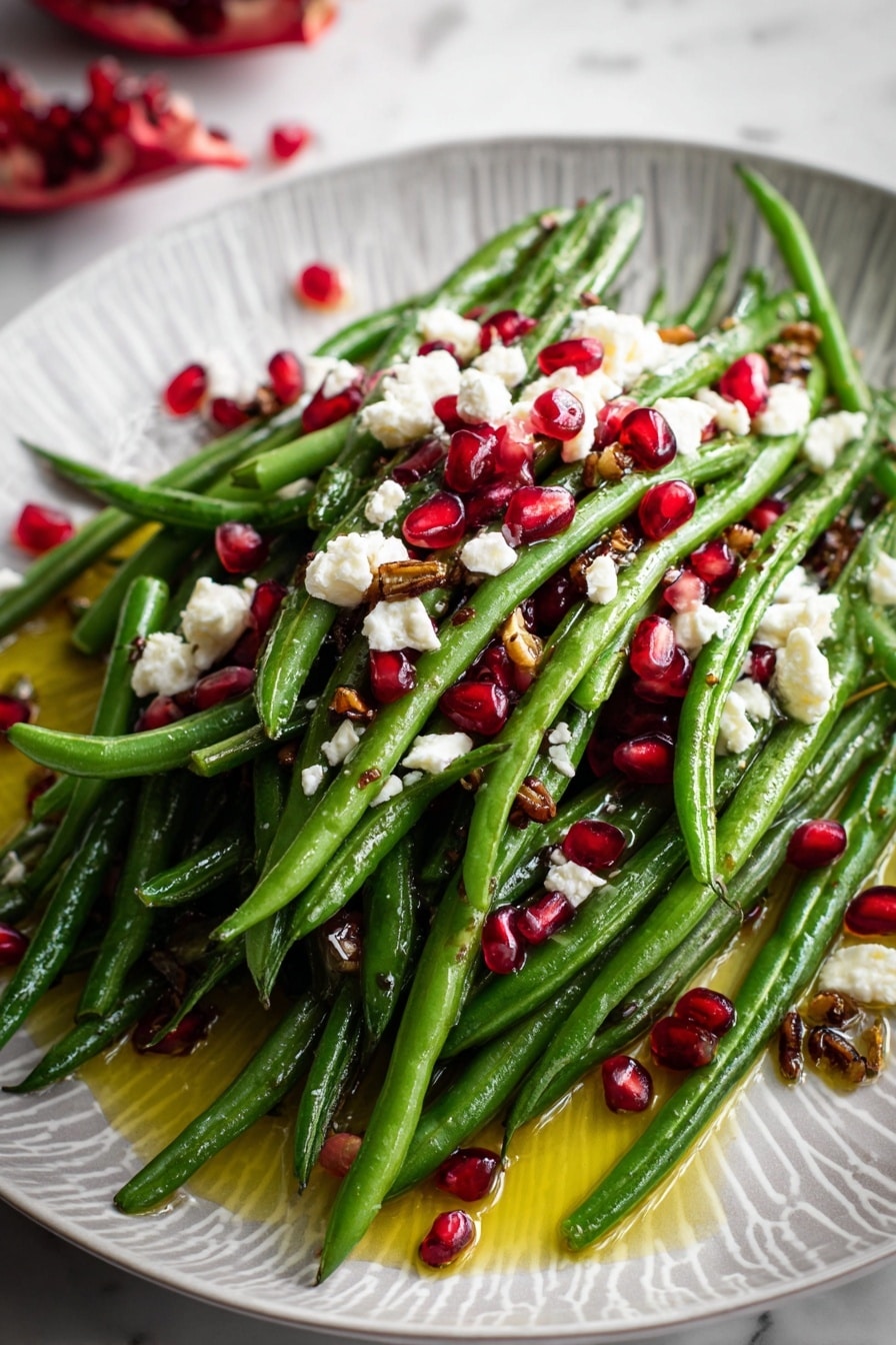 A white oval plate with a light gray geometric pattern holds a fresh green bean salad arranged in a loose pile. The green beans are bright and shiny, forming the main base layer. Scattered evenly on top are small, bright red pomegranate seeds that add pops of color. Clumps of white cheese are spread on the green beans in small pieces, adding a soft texture. Thin, dark brown crispy bits are sprinkled over everything. A yellow oily dressing pools around the edges of the plate. The whole scene is set on a white marbled surface, with a small piece of pomegranate to the side and a soft lavender cloth napkin nearby. photo taken with an iphone --ar 2:3 --v 7 - Maple Mustard Green Beans with Pomegranate and Goat Cheese, green bean side dish with pomegranate and goat cheese, healthy green bean recipes, flavorful vegetable sides, easy festive green beans