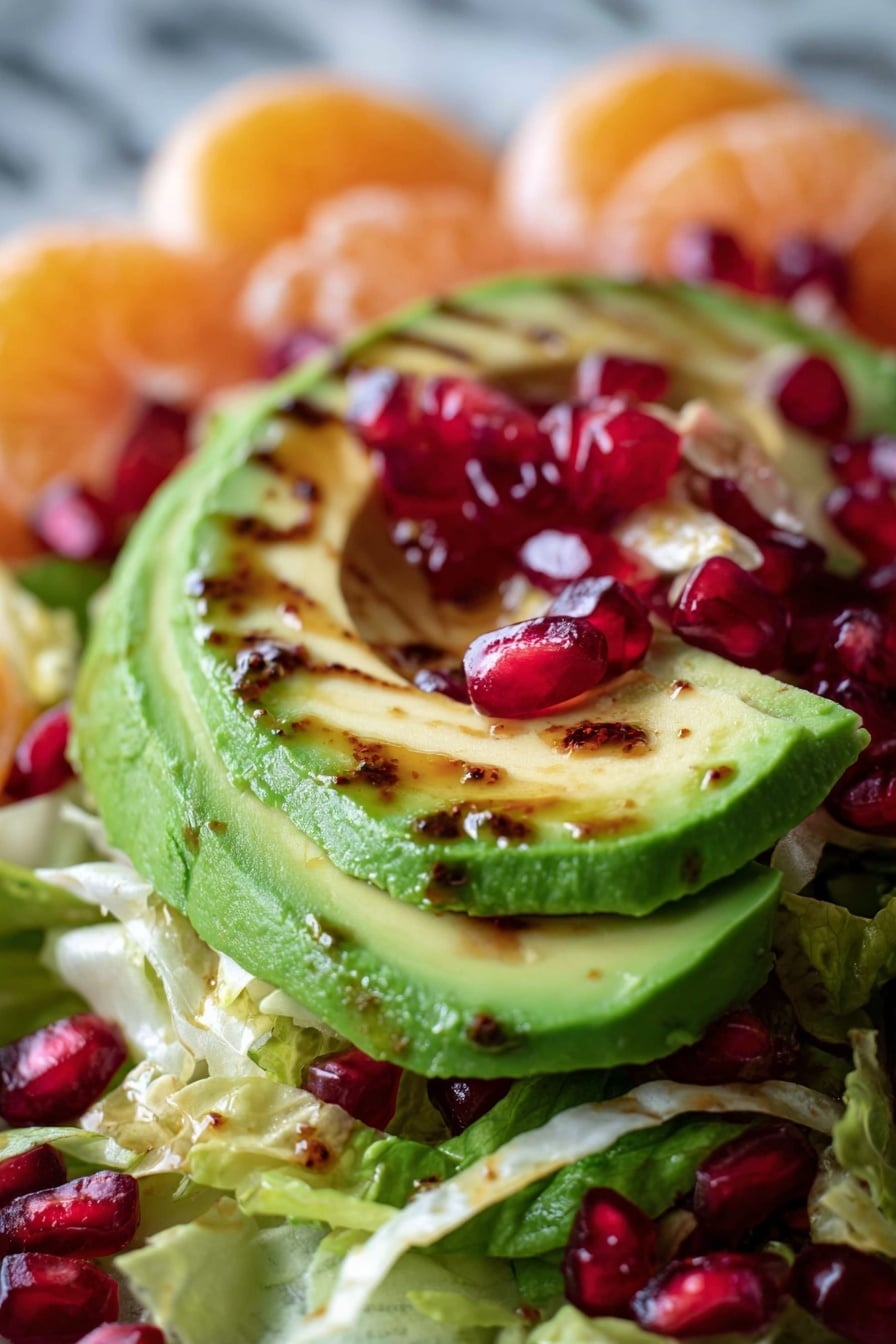 A white plate holds a fresh salad arranged in layers, starting with a base of finely shredded green Brussels sprouts. On top, there are bright orange slices scattered evenly, each slice glazed with a light golden shine. Three halves of avocado with smooth, pale green flesh sit prominently, each filled with dark balsamic glaze. Small, shiny red pomegranate seeds are sprinkled generously across the salad, adding pops of color and texture. A golden spoon rests on the edge of the plate, and the whole scene is set against a white marbled surface with a quarter of an orange visible nearby. photo taken with an iphone --ar 2:3 --v 7 - Citrus Brussels Pomegranate Salad, healthy citrus salad, easy Brussels sprouts salad, festive fruit and vegetable salad, quick side salad recipes