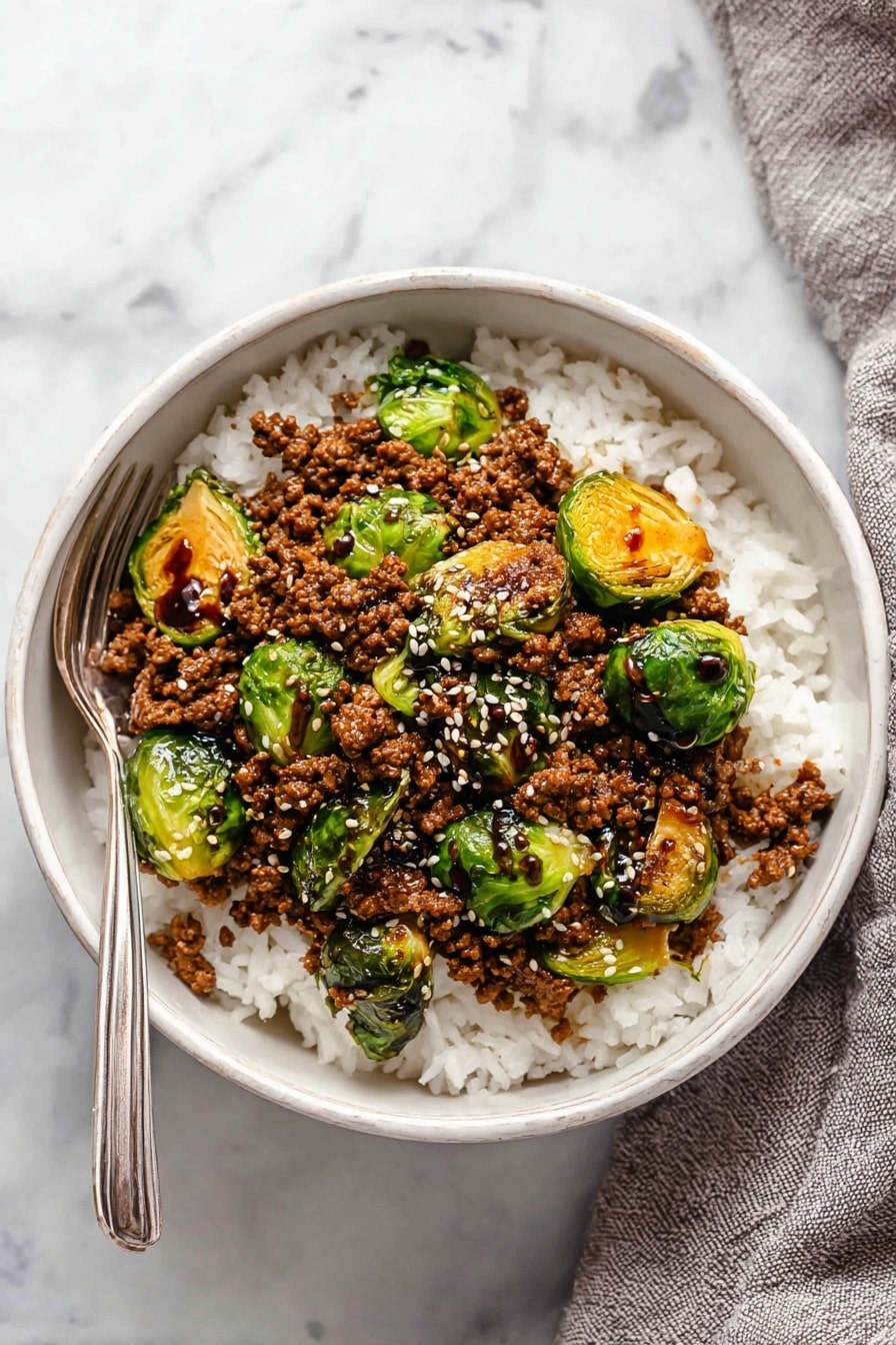 A black pan filled with cooked ground meat and halved Brussels sprouts scattered evenly across the top, with some leaves slightly charred and curled from cooking. The meat is brown and crumbly, forming the base layer, while the Brussels sprouts add green and yellow hues with some golden brown edges. White sesame seeds are sprinkled lightly over the dish, adding texture and small white highlights. The pan rests on a white marbled surface seen in the background, with a gray cloth partially visible to the side. Photo taken with an iphone --ar 2:3 --v 7 - Ground Beef and Brussels Sprouts Stir-Fry with Sweet Chili and Lime, healthy ground beef stir-fry, quick weeknight dinner recipe, easy stir-fry with Brussels sprouts, flavor-packed beef stir-fry