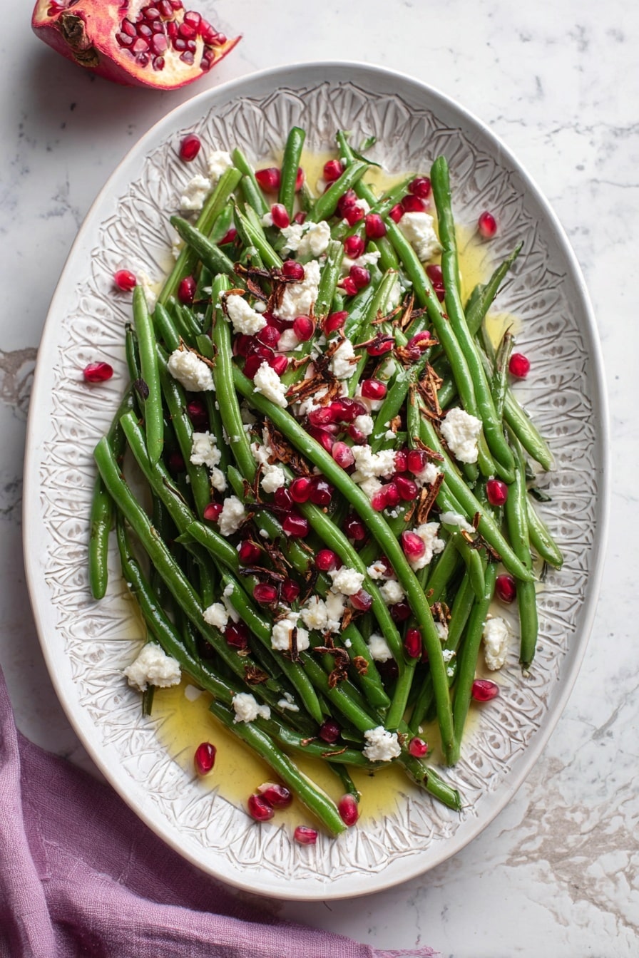 The dish is a stack of bright green beans piled high on a white plate with a subtle gray pattern. Scattered on top are small white pieces of crumbly cheese, clusters of shiny deep red pomegranate seeds, and small crunchy brown bits. A pool of golden oil surrounds the green beans at the bottom, adding shine to the whole dish. The plate is placed on a white marbled surface with a few pomegranate seeds partly visible in the top left corner. The colors are fresh and vibrant, showing the mix of soft, crunchy, and juicy textures. photo taken with an iphone --ar 2:3 --v 7 - Maple Mustard Green Beans with Pomegranate and Goat Cheese, green bean side dish with pomegranate and goat cheese, healthy green bean recipes, flavorful vegetable sides, easy festive green beans