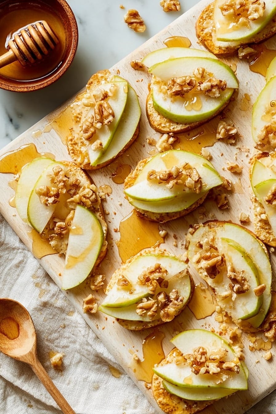 Thin golden toasted cheese rounds form the base layer, each topped with two or three thin, pale green and white pear slices arranged slightly overlapping. On top of the pears are small clusters of light brown chopped walnuts scattered unevenly. A drizzle of amber honey glistens over everything, adding a sticky shine. The snacks are spread randomly over a light wooden board with some crumbs and drops of honey visible. In the corner, a small brown bowl with honey and a wooden honey dipper rests on a white marbled textured surface, along with a white cloth. Photo taken with an iphone --ar 2:3 --v 7 - Parmesan Crusted Crostini with Pear, Walnuts & Hot Honey, pear crostini appetizer, savory sweet crostini, easy elegant appetizer, crunchy cheese crostini
