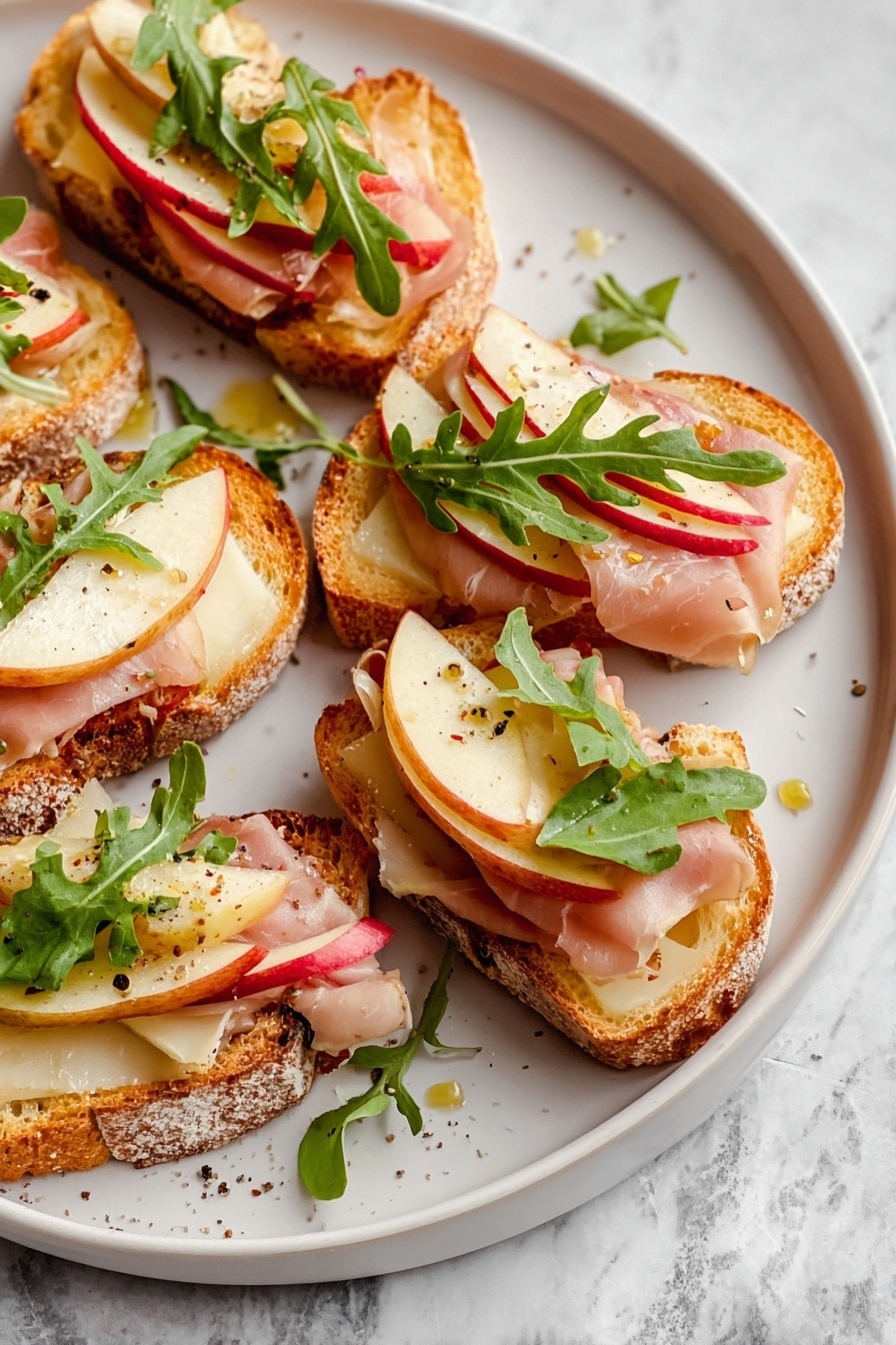 This image shows several pieces of toasted bread slices arranged on crumpled white paper over a white marbled surface. Each slice has three layers: a base layer of melted cheese that looks creamy and yellowish, a middle layer of thin apple slices with red skins, and a top layer of pinkish ham curls draped neatly. Some slices have green arugula leaves scattered on top, adding fresh color. There are small drops of honey scattered on the paper around the toasts. To the right, there is a small white bowl with amber honey inside and a silver spoon resting on the edge. The scene looks bright and inviting. photo taken with an iphone --ar 2:3 --v 7 - Apple & Brie Crostini with Hot Honey, Apple Brie Crostini appetizer, easy fruit and cheese crostini, hot honey fruit appetizer, elegant snack ideas