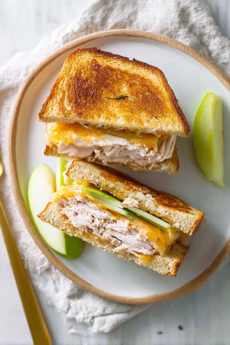The image shows two sandwich halves stacked on a wooden board with a toasted golden-brown crust on the outside layer. Inside, the sandwich has three visible layers: a light brown toasted bread slice at the base, a thick layer of white cooked turkey meat with a soft texture in the middle, and a layer of melted yellow cheese with a smooth, slightly shiny surface. Towards the top inside, there are green apple slices adding a fresh, crisp texture, visible in between the turkey meat. Around the board, there are a few fresh green leaves, green apple slices, a red and yellow apple, and two silver forks on a white marbled surface with a green and white checkered cloth in the background. photo taken with an iphone --ar 2:3 --v 7 - Apple Grilled Cheese with Turkey, savory turkey grilled cheese, apple and cheese sandwich, quick lunch recipes, easy gourmet sandwiches
