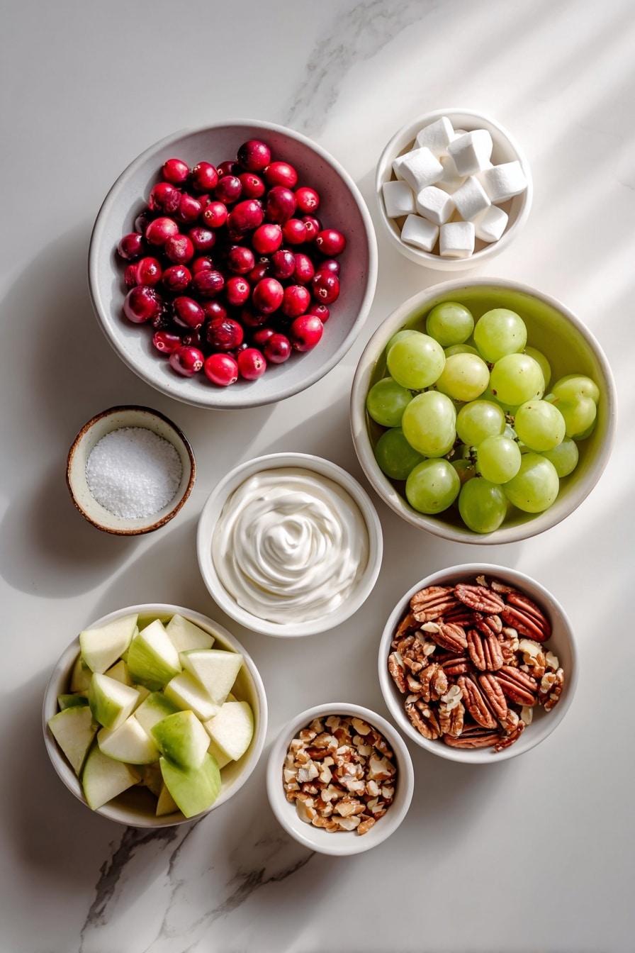 Flat lay of fresh whole cranberries scattered on a simple white ceramic plate, a small white bowl filled with miniature white marshmallows, a small white bowl holding crystalline white granulated sugar, freshly diced unpeeled tart apples arranged neatly on a white ceramic dish, halved bright green grapes in a small white bowl, a small white bowl with chopped mixed nuts showing walnut and pecan pieces, a tiny white bowl containing fine white salt, and a delicate swirl of freshly whipped cream in a small white ceramic bowl, placed on a clean white marble surface, soft natural light, photo taken with an iPhone, professional food photography style, fresh ingredients, white ceramic bowls, no bottles, no duplicates, no utensils, no packaging --ar 2:3 --v 7 - Cranberry Fluff, Cranberry Fluff Dessert, Easy Cranberry Fluff, Holiday Cranberry Fluff, Creamy Fruit Fluff